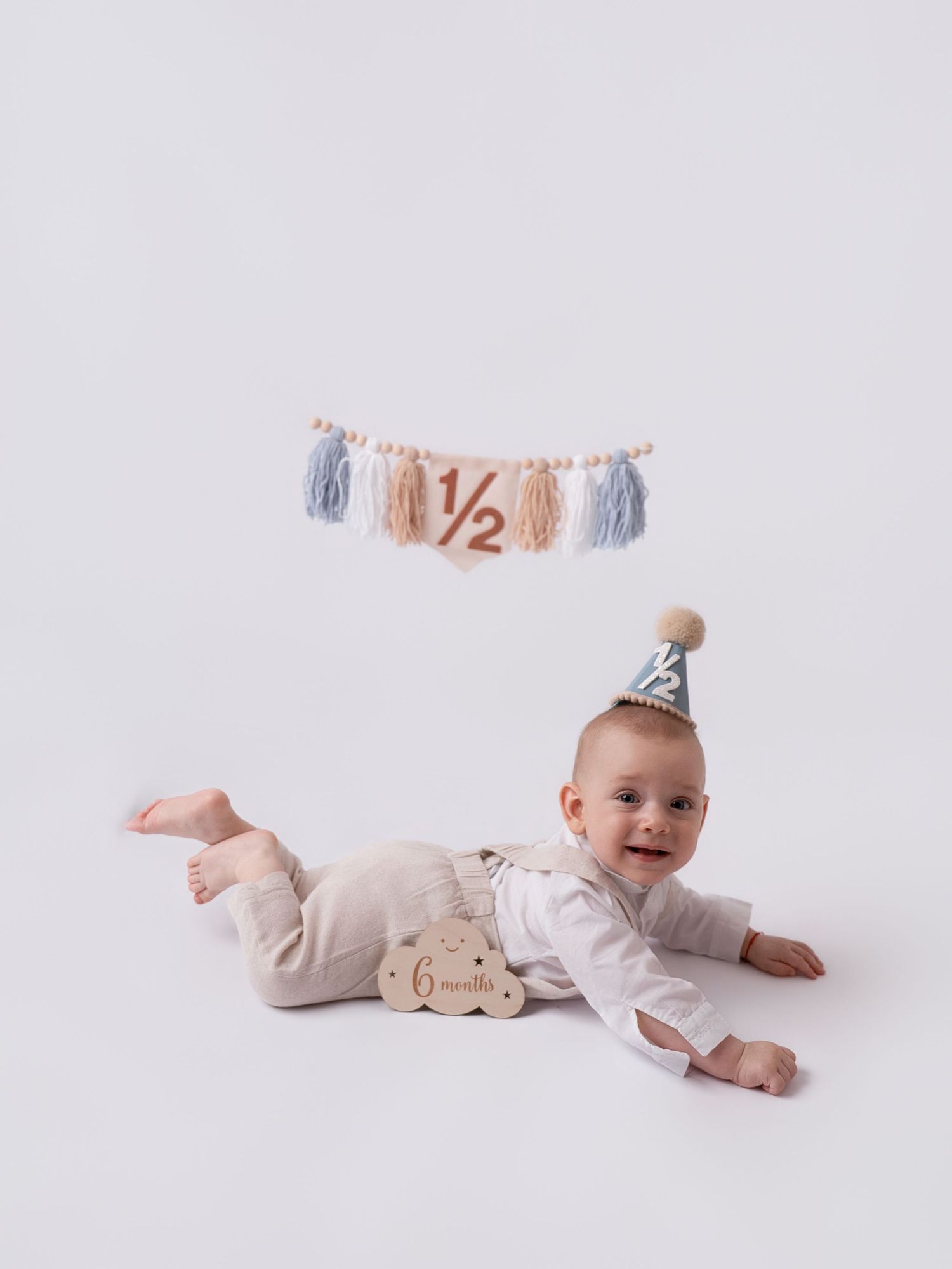 Baby in party hat lying on stomach celebrating 6-month half birthday with tassel banner and wooden milestone block.