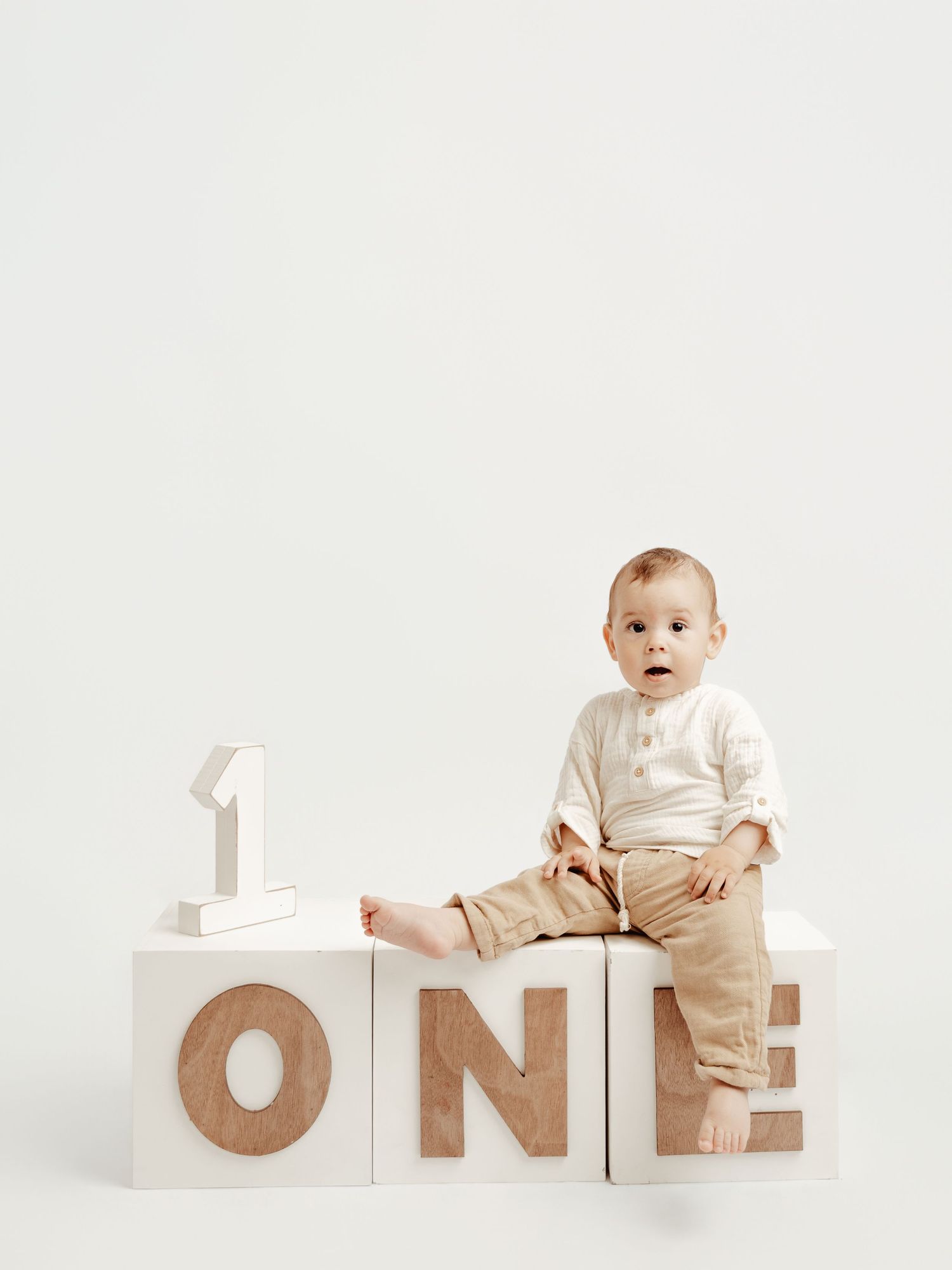 Baby sitting on white blocks spelling ONE for a first birthday milestone photo.