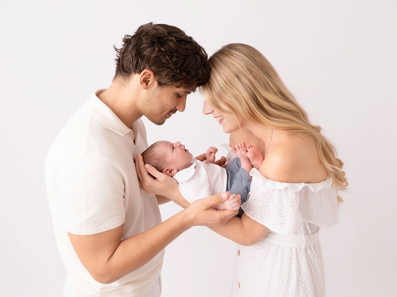 New parents tenderly holding their newborn baby together against a white studio background.