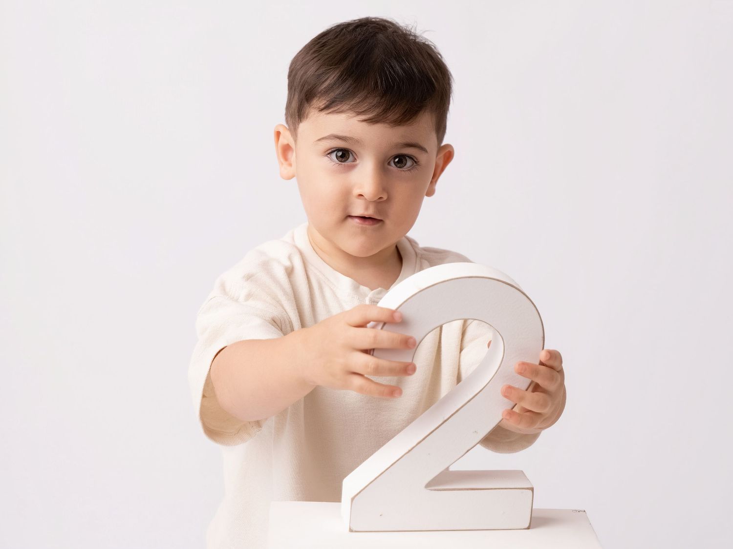 Cute toddler boy holding a large number 2 sign, perfect for a second birthday photo shoot.