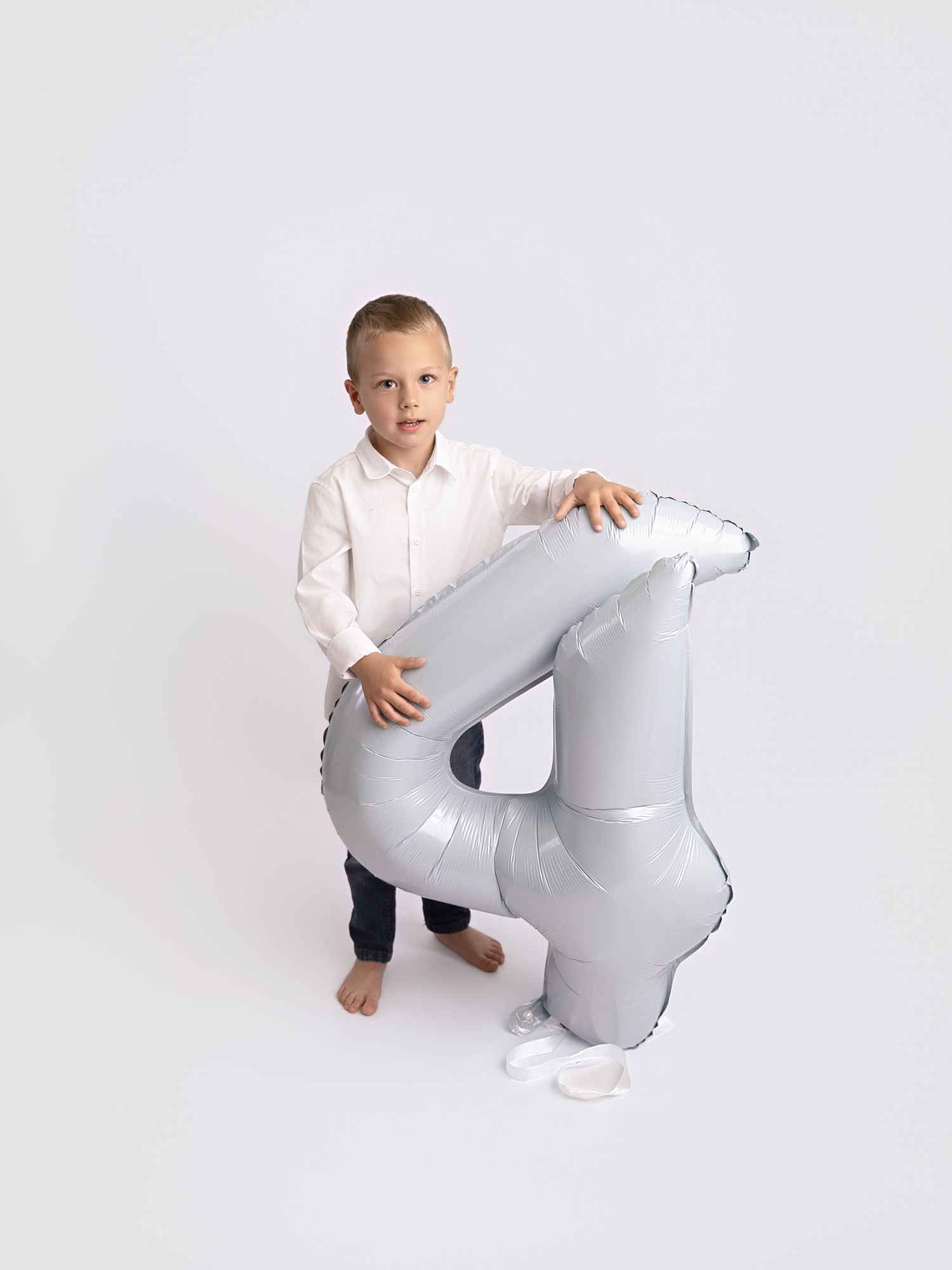 Young boy in white shirt holding a large silver number 4 balloon, celebrating his 4th birthday.