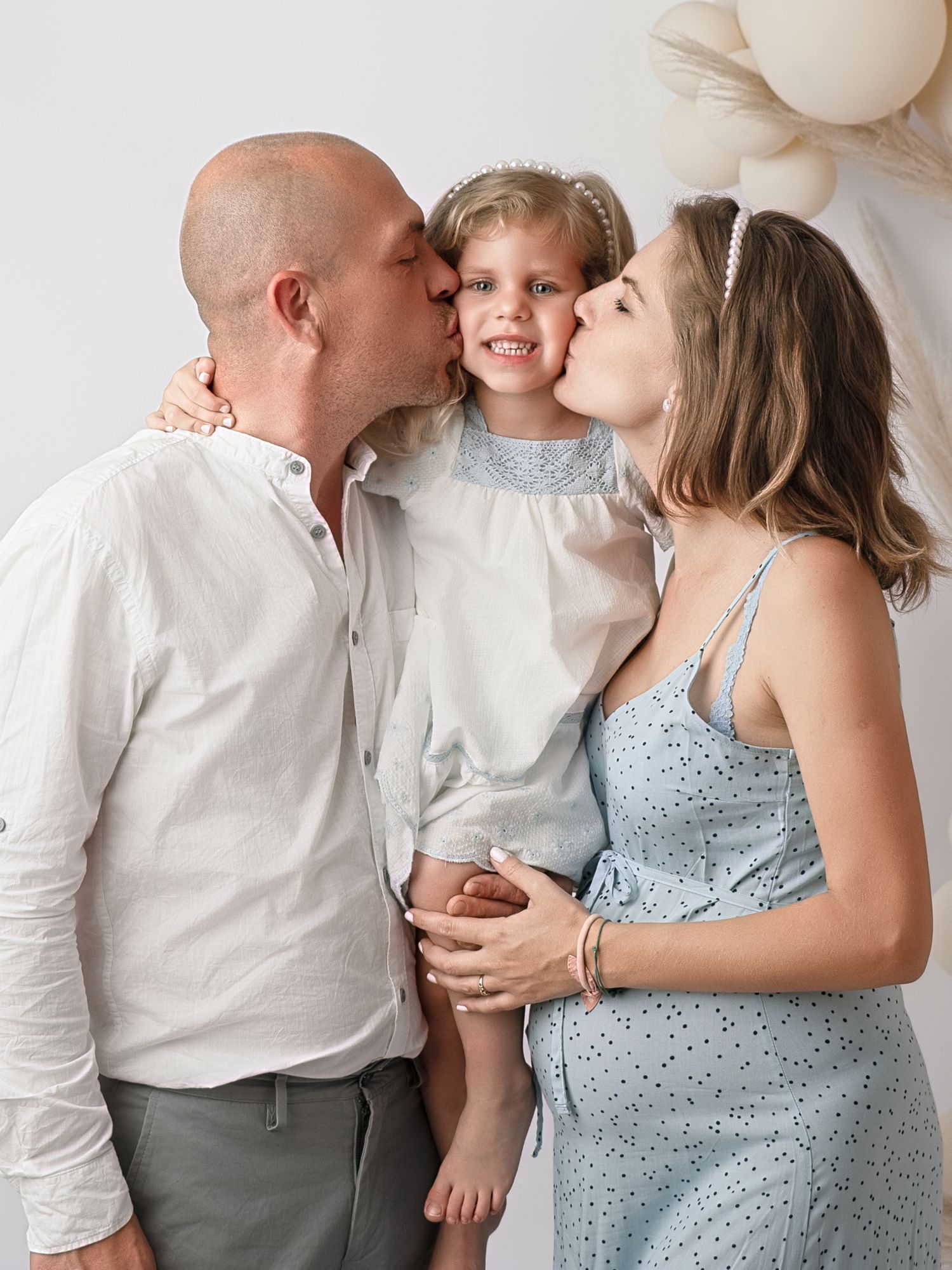 A couple kisses their smiling young daughter on the cheeks during a family portrait session.