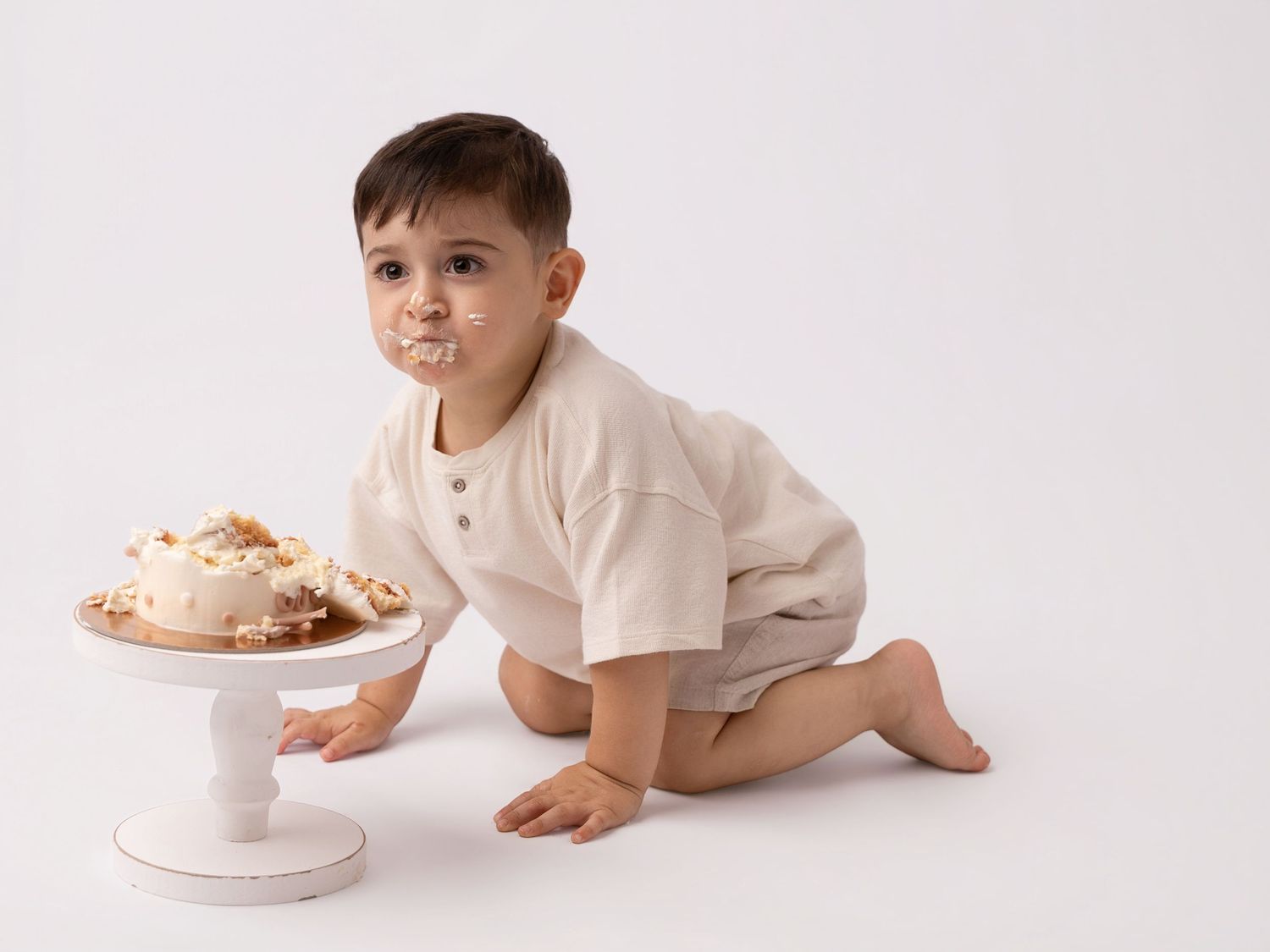 Toddler boy with cake on his face during a cake smash birthday photo session.