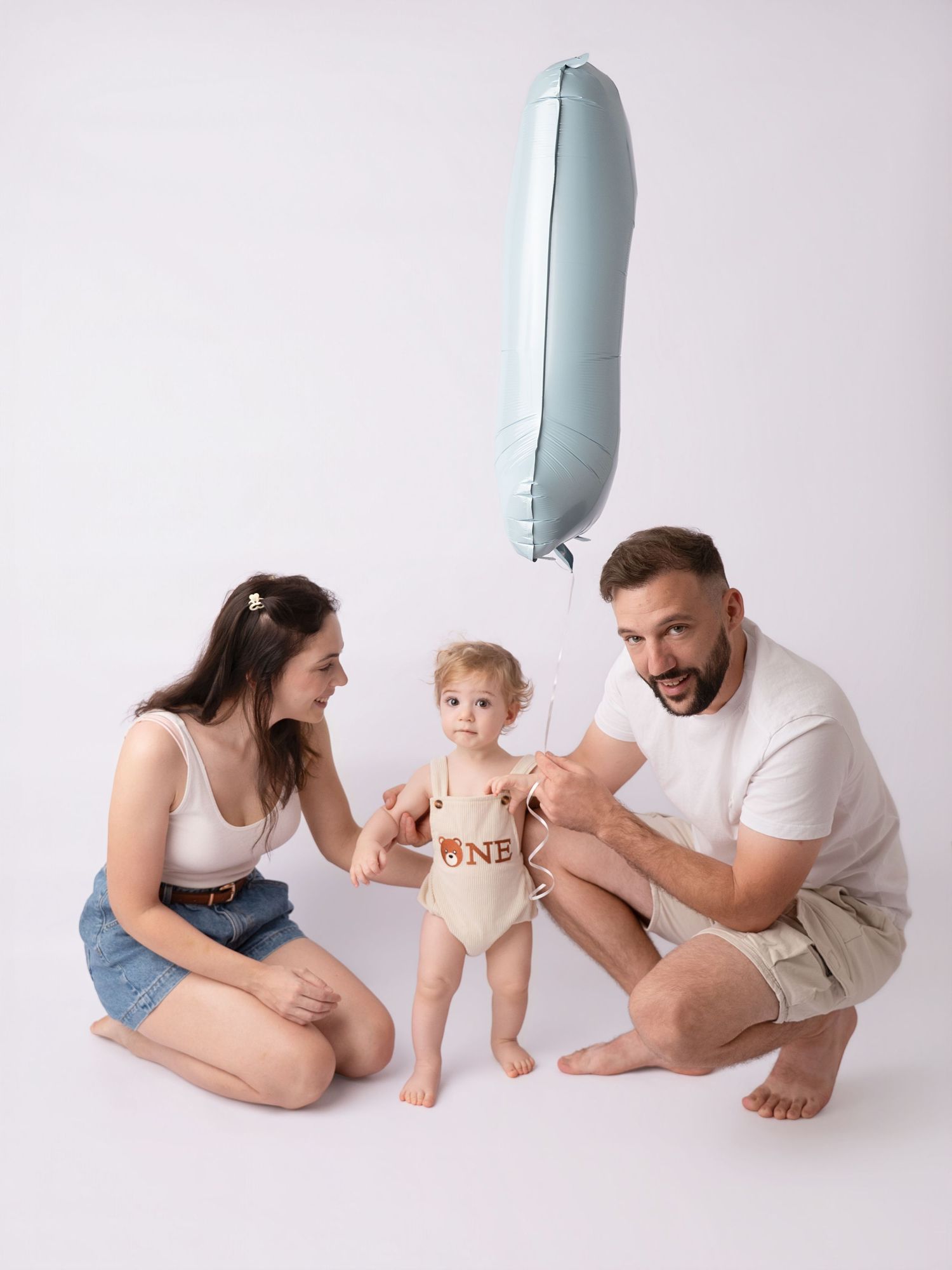 Young family with baby holding blue number one balloon celebrating first birthday portrait.