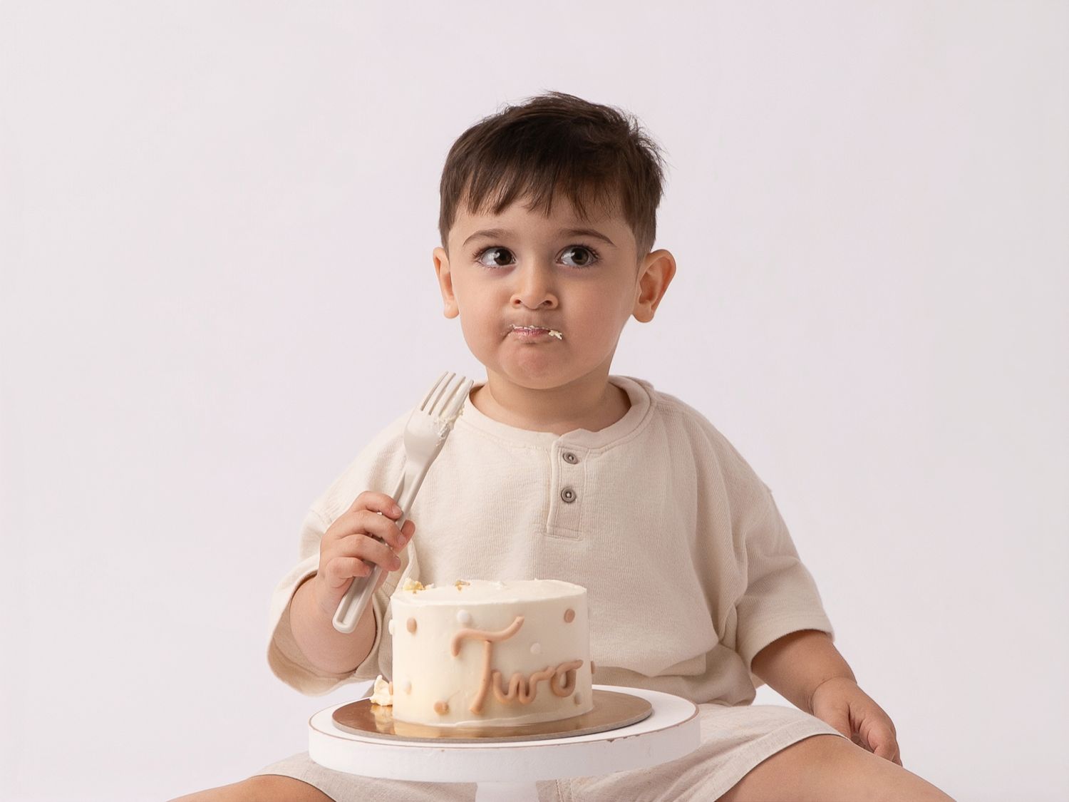 Cute toddler boy eating birthday cake with a fork, smiling with frosting on his face, white background.