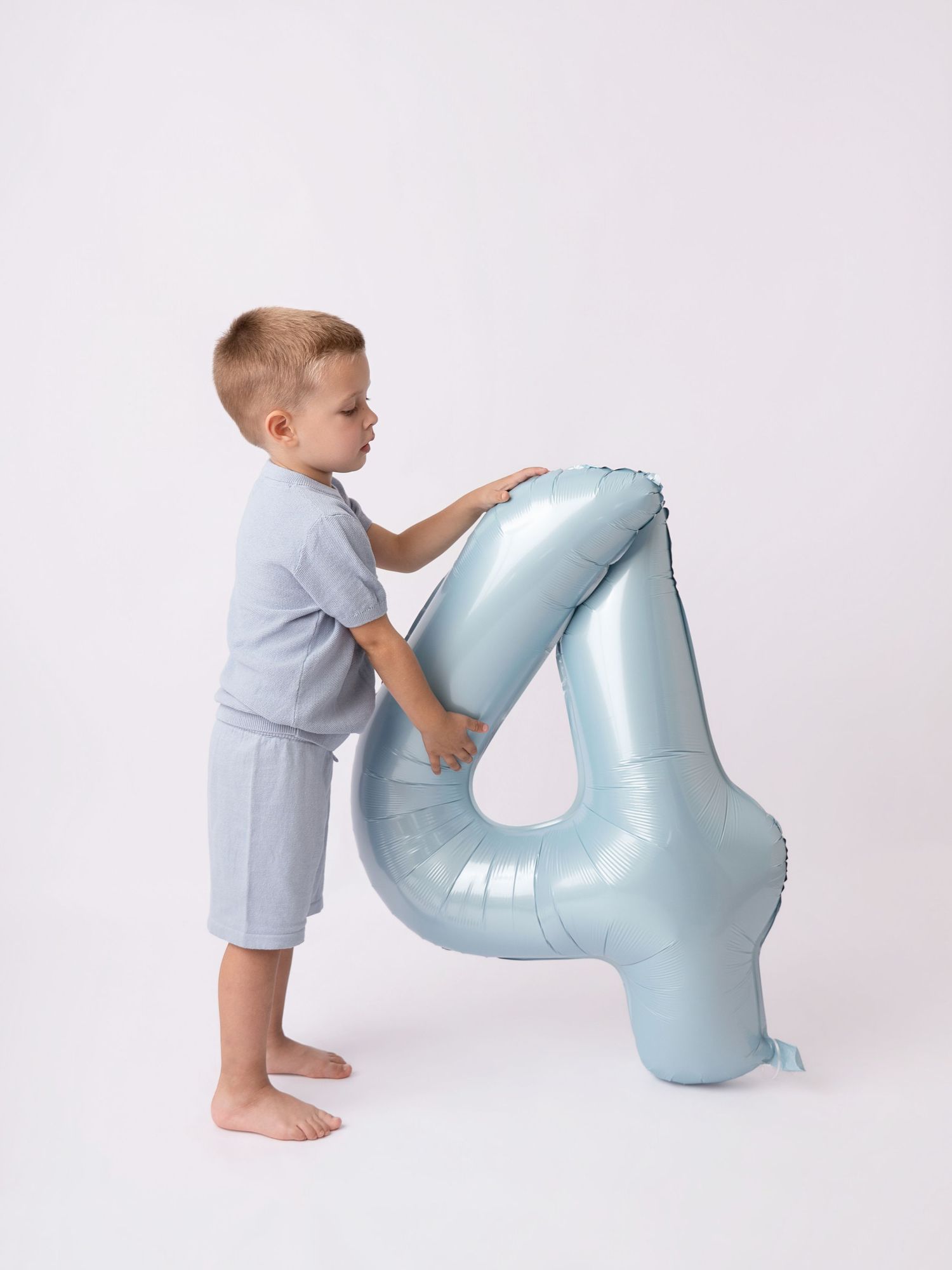 Young boy holding a large light blue number 4 foil balloon against a white background.