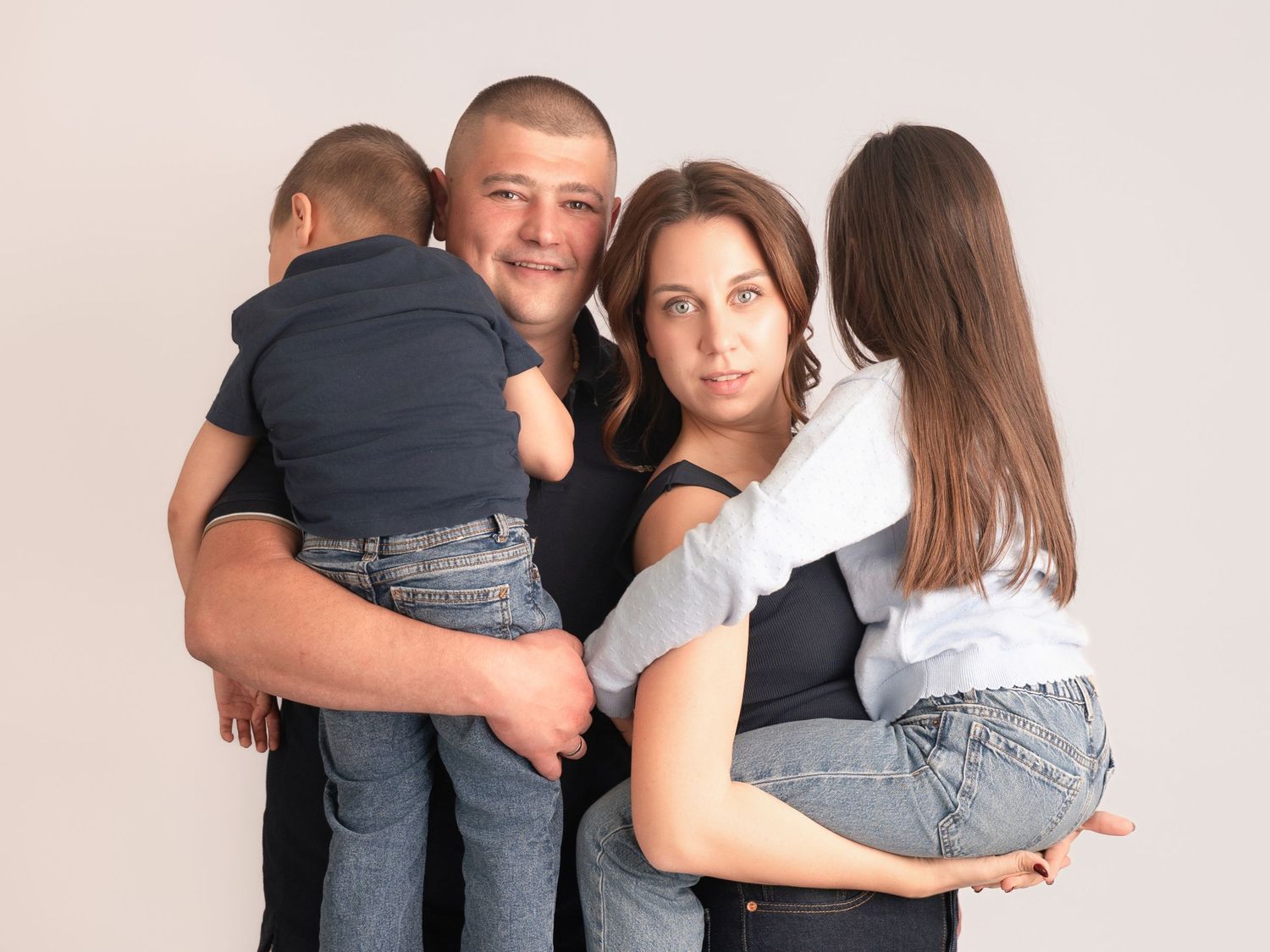 A happy family of four posing for a portrait, with parents each holding a young child against a light background.