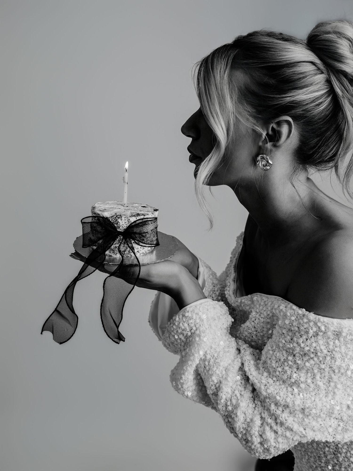 Black and white photo of blonde woman in white dress blowing out birthday cake candle.