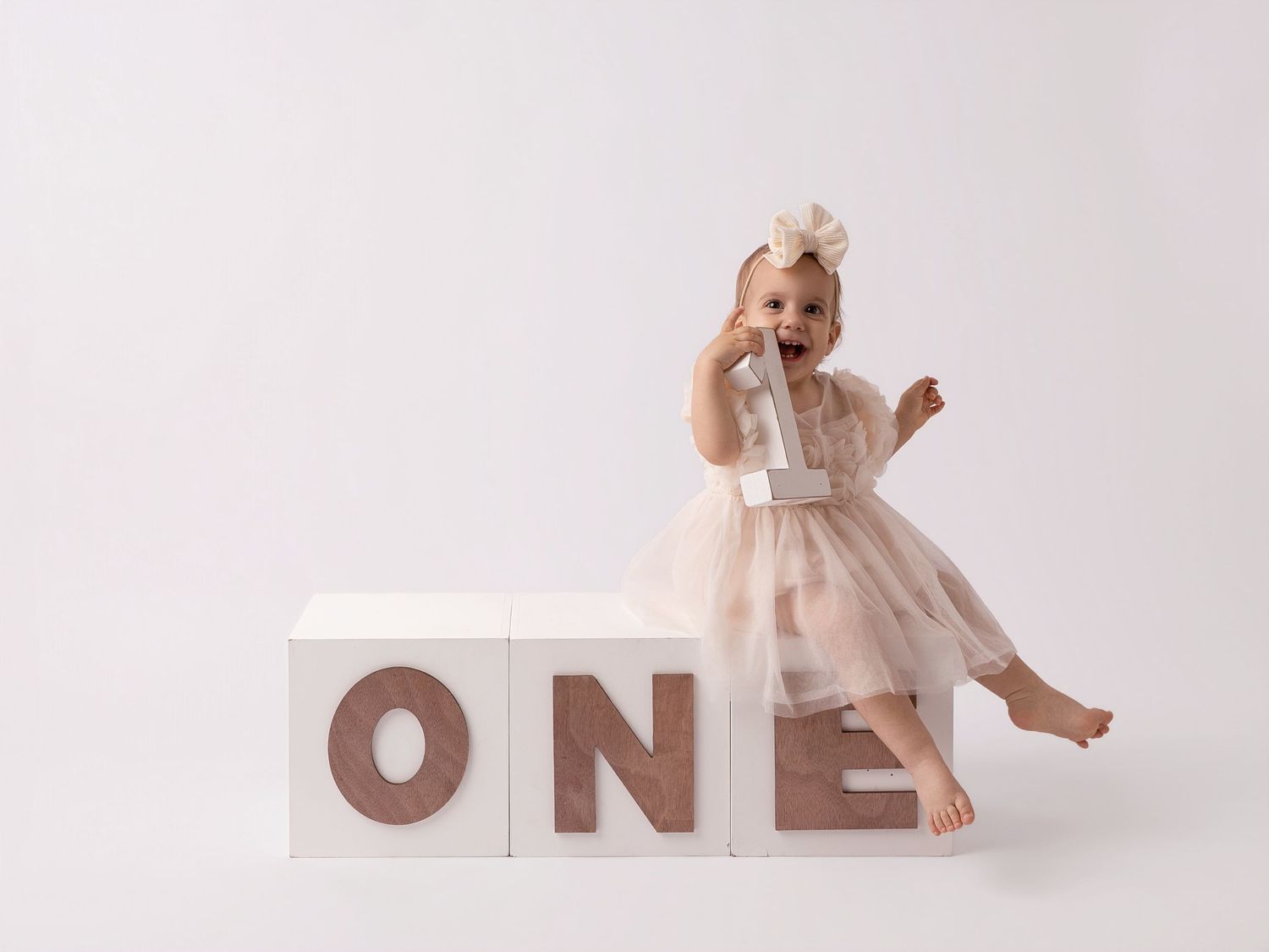 A baby girl in a tutu dress sits against white ONE blocks for her first birthday photo session.