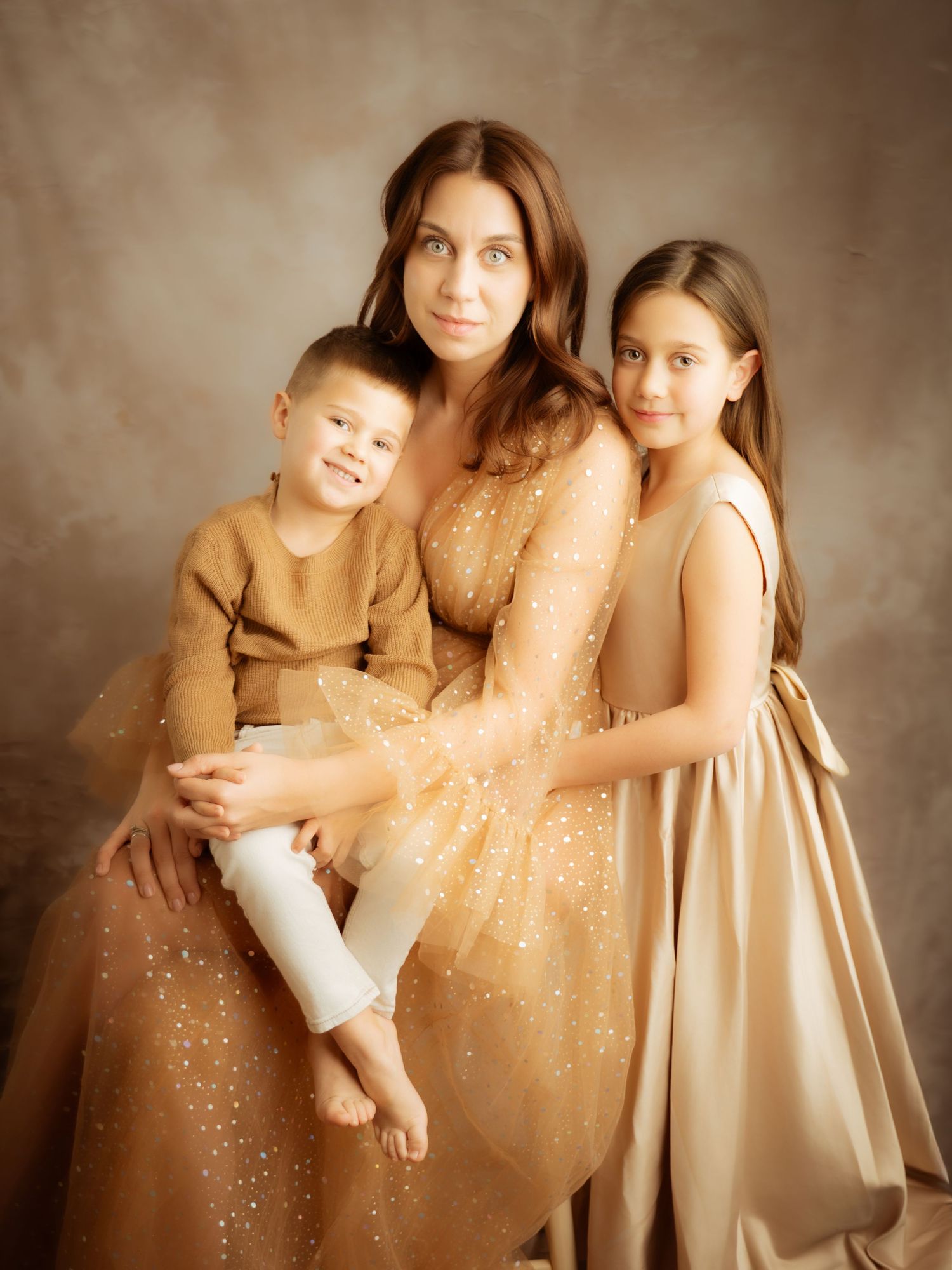 Mother in gold sparkle dress posing with her two children in a warm-toned professional family studio portrait.
