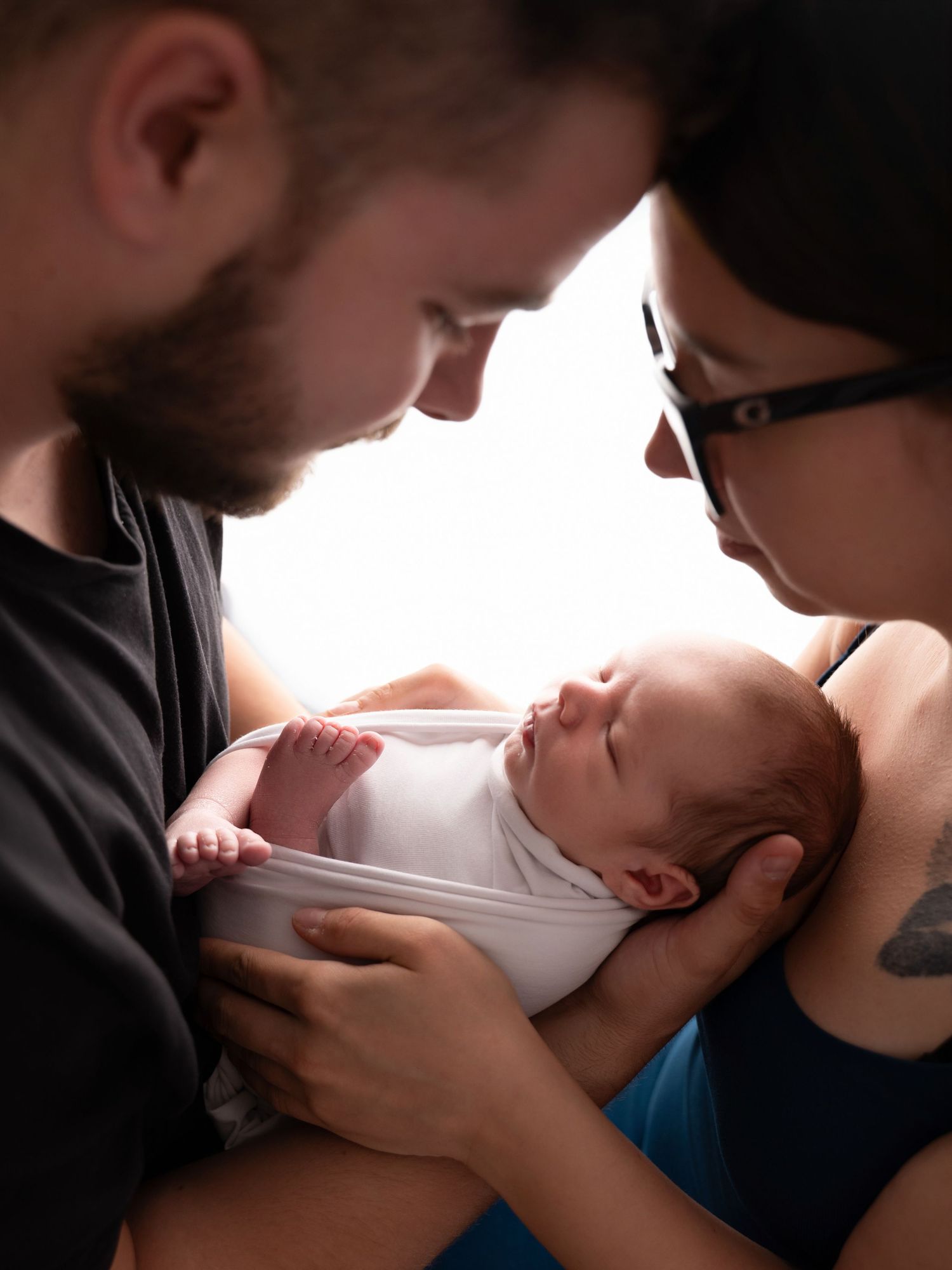 A couple lovingly gazes at their newborn baby wrapped in white, sharing a tender family moment.