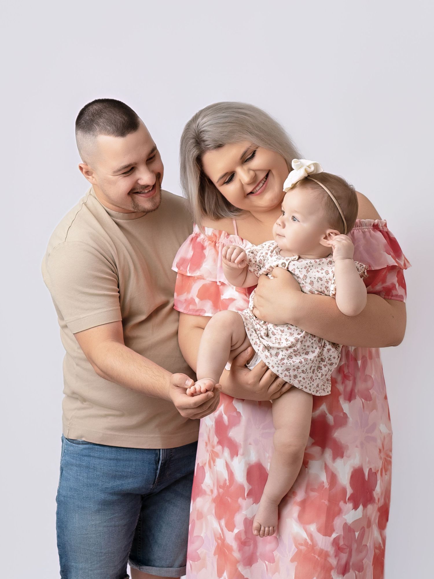 Smiling parents in casual floral and neutral outfits admire their baby girl in a studio portrait.