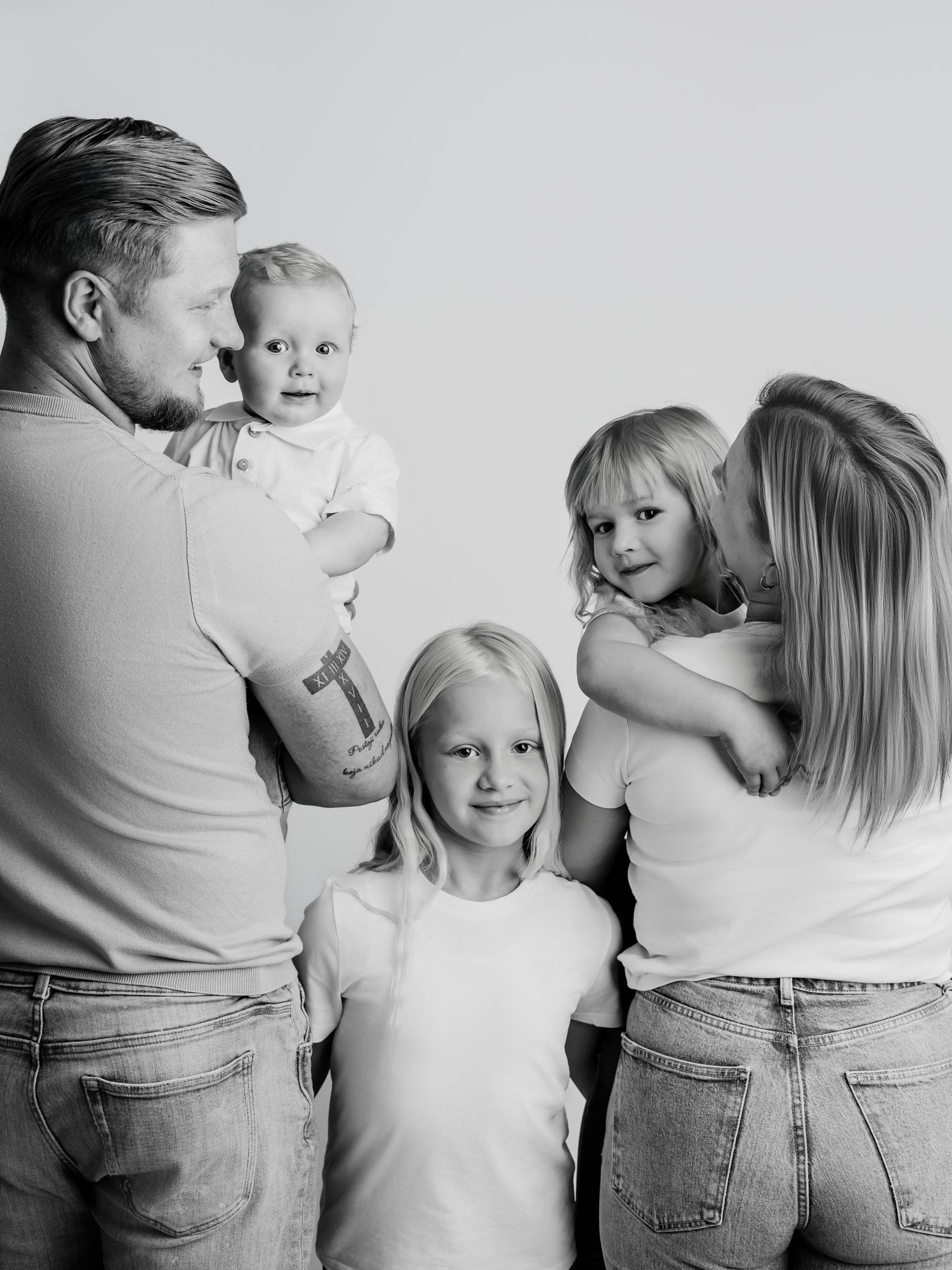A black and white family portrait of parents lovingly holding their three young children in a studio.