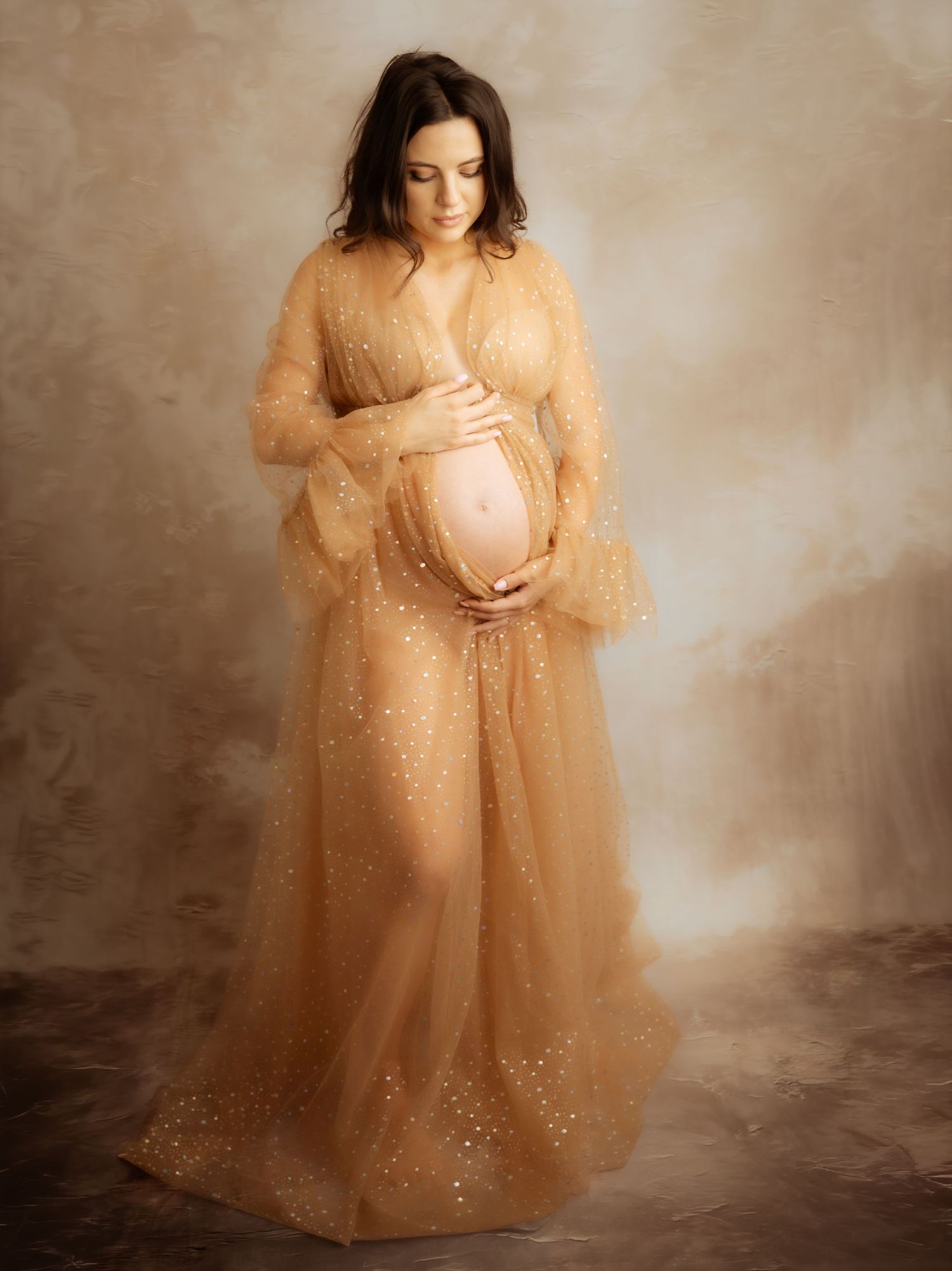 Pregnant woman in gold sparkle tulle maternity gown holding baby bump.