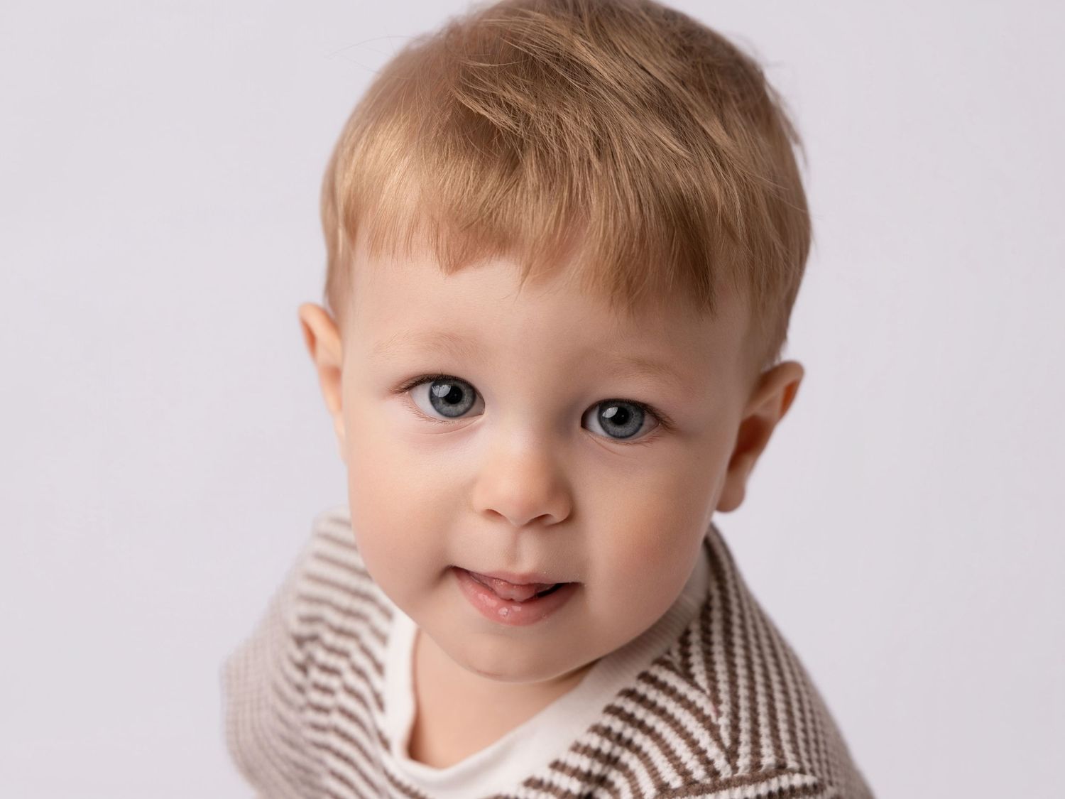 Adorable blonde toddler with blue eyes wearing a striped outfit, posing for a professional portrait photo.
