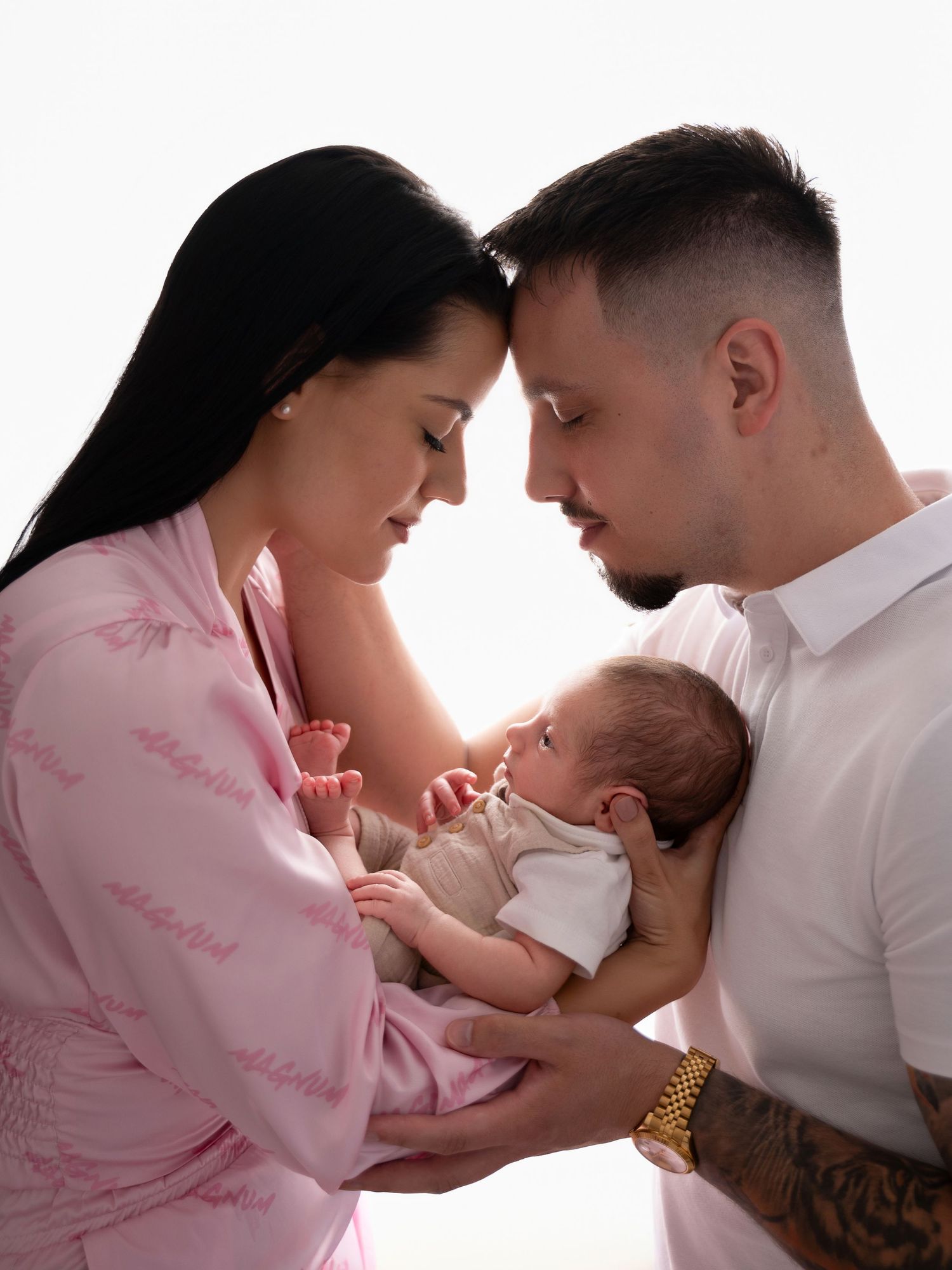 New parents tenderly holding their newborn baby, mother in pink robe and father with tattoos, sharing an intimate moment.