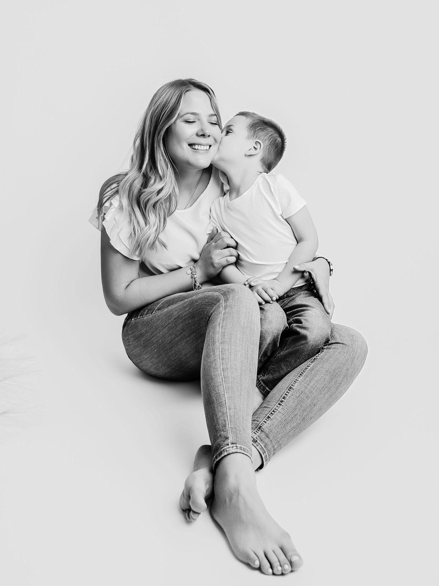 Black and white photo of a mother smiling as her young toddler gives her a kiss on the cheek.
