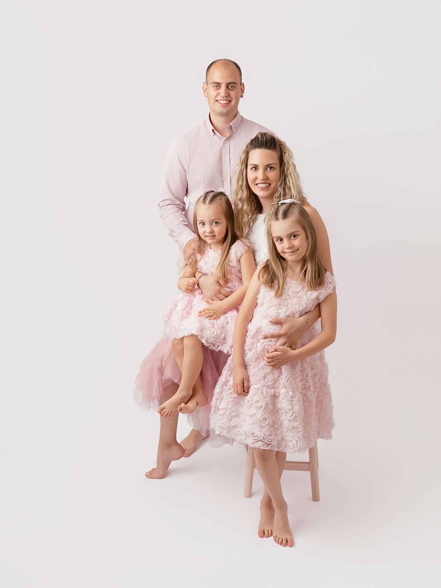 Family of four wearing coordinated pink outfits posing for a professional studio portrait.