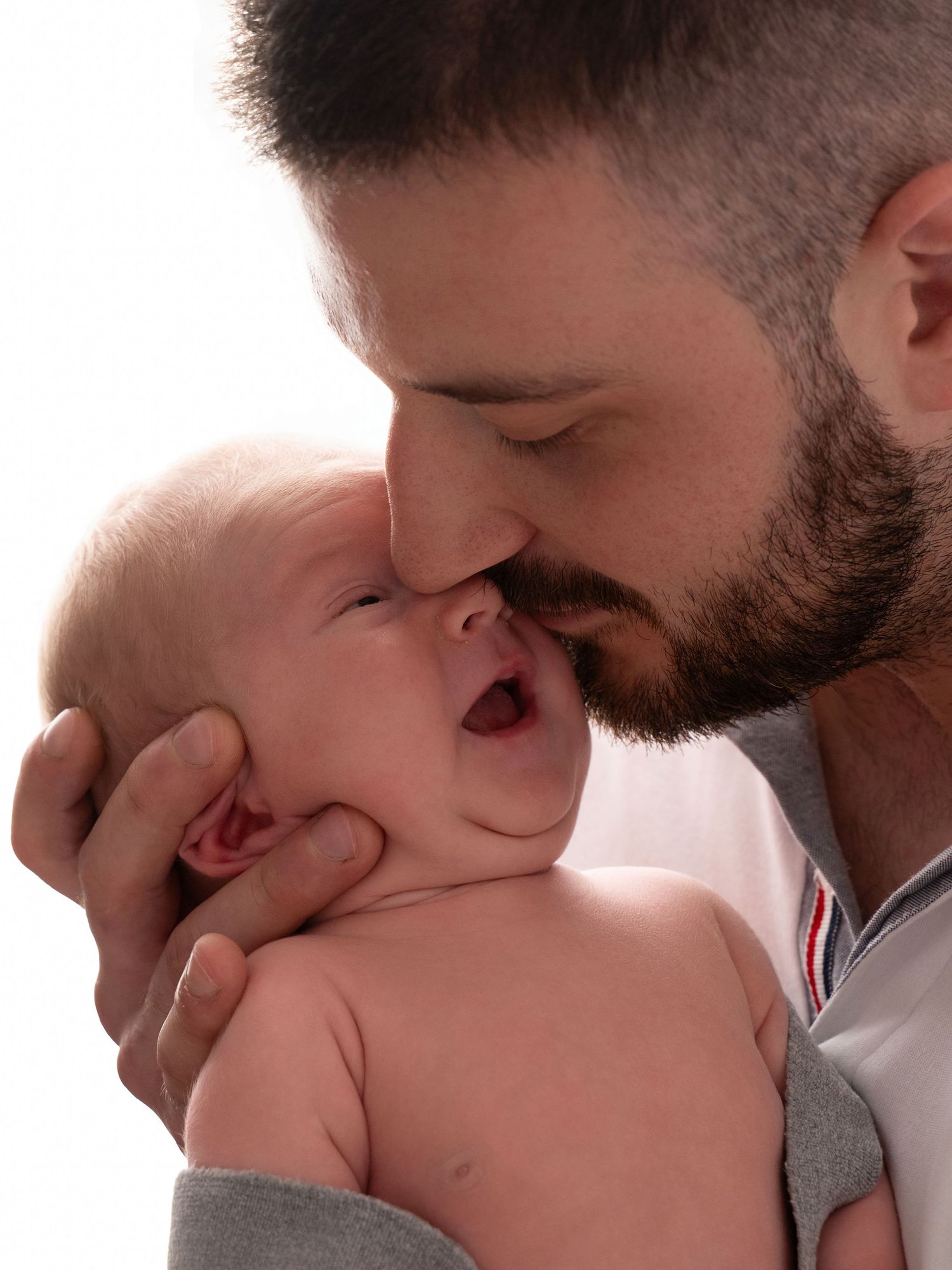 Bearded father tenderly kissing his newborn baby, cradling the infant gently while the baby yawns.