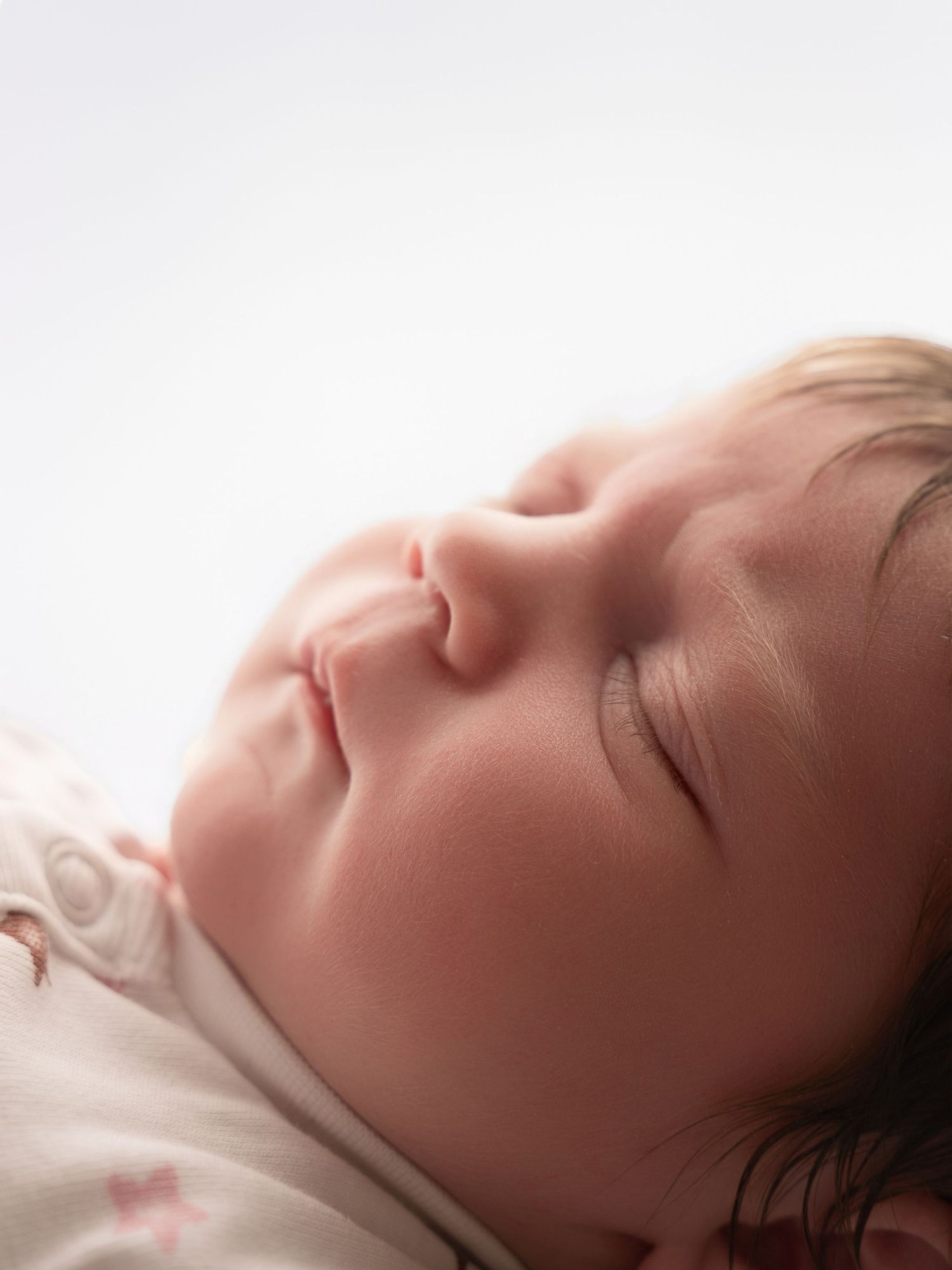 Extreme close-up of sleeping newborn babys face with soft skin and dark hair against white background.