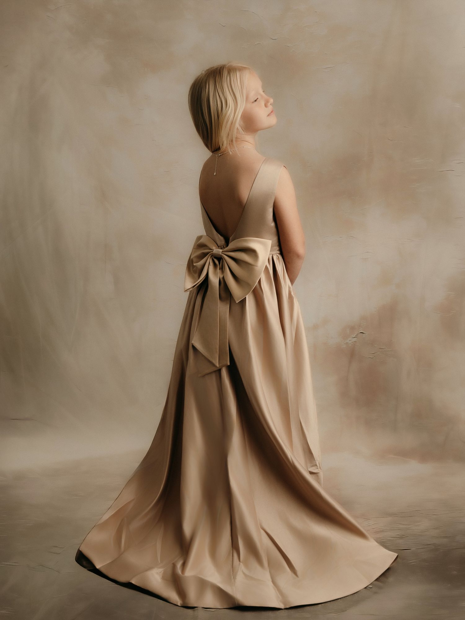 Girl in a stunning backless champagne satin gown with oversized bow and dramatic train, studio portrait.
