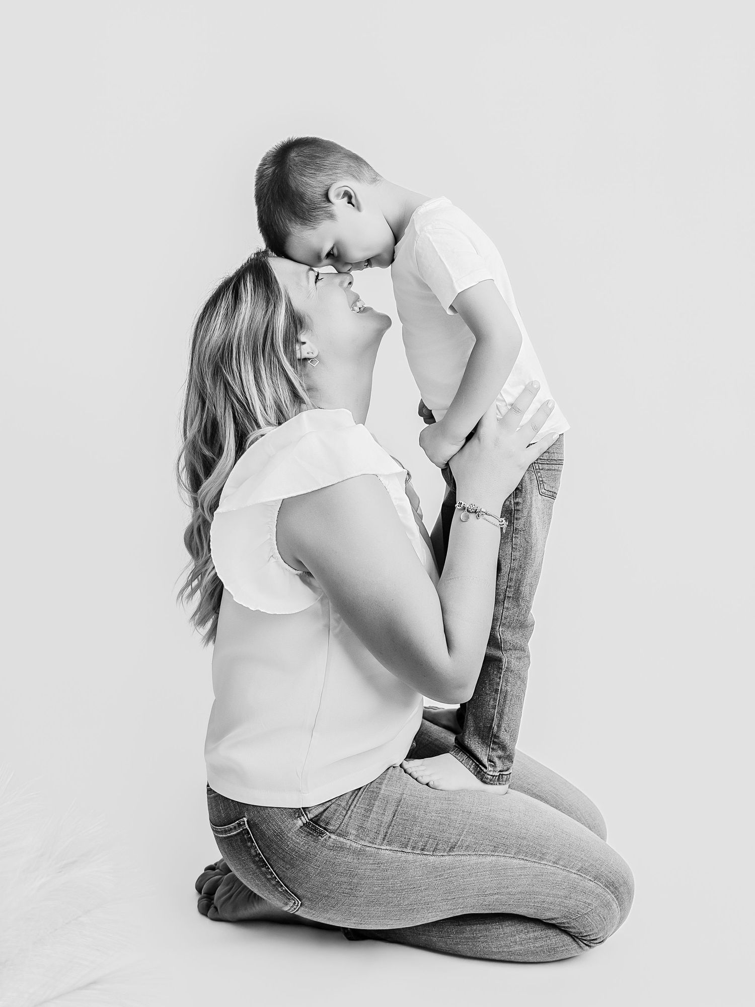 Black and white image of a mother kneeling and touching foreheads with her young son in a tender moment.