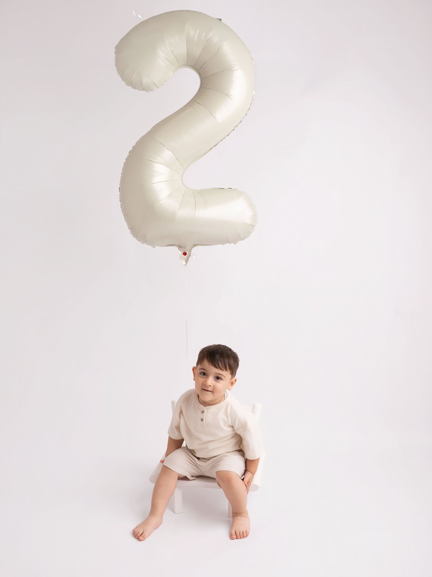 Baby boy sitting under a large number 2 balloon for his second birthday photoshoot.