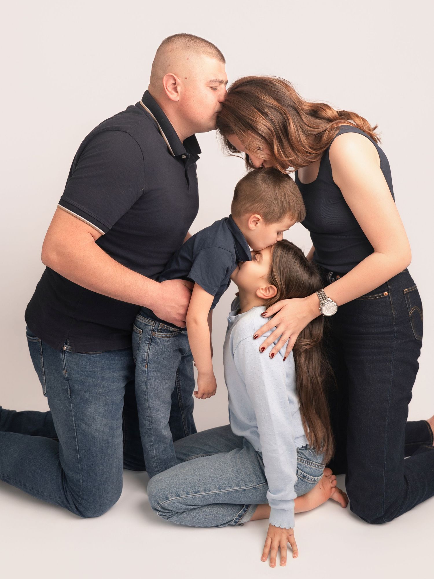 Family of four sharing a tender group hug during a professional studio photo session.