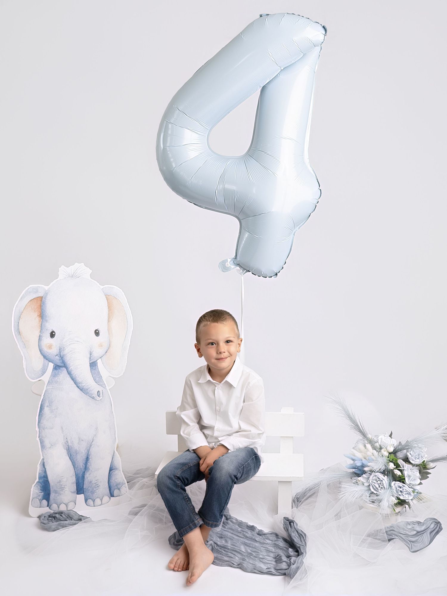 Boy in white shirt sits beside elephant cutout with blue number 4 balloon for 4th birthday photo.