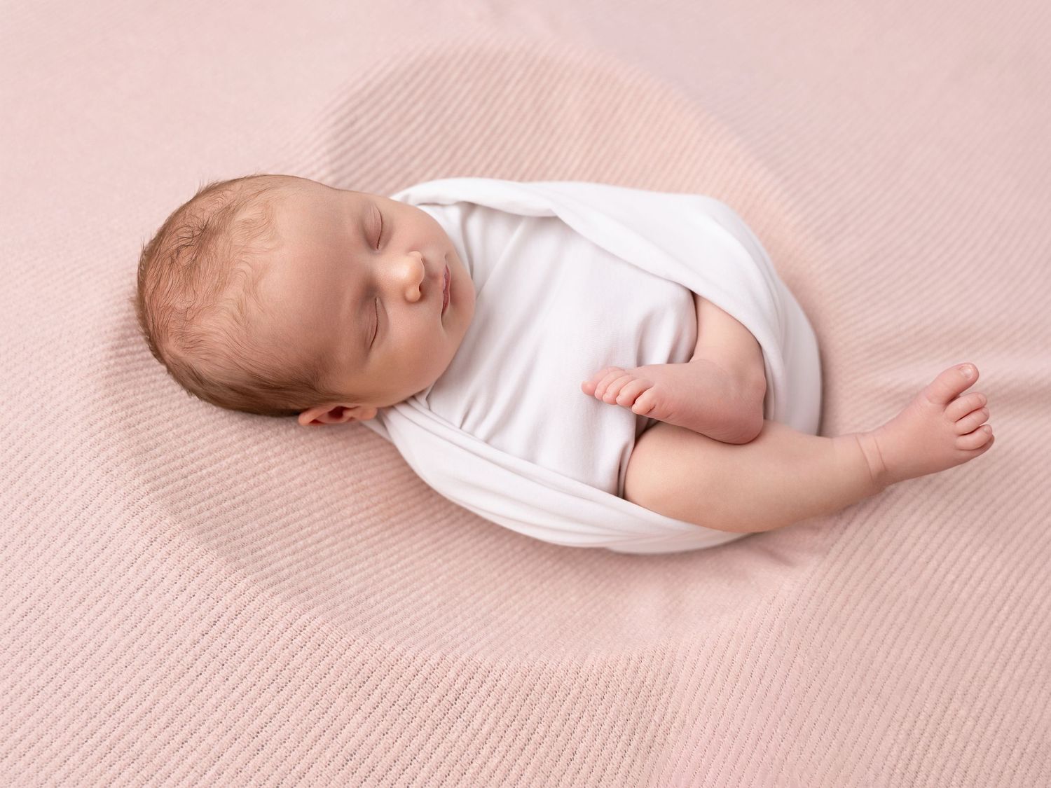 Peaceful newborn baby sleeping on a soft pink blanket wearing a white onesie, perfect for nursery inspiration.