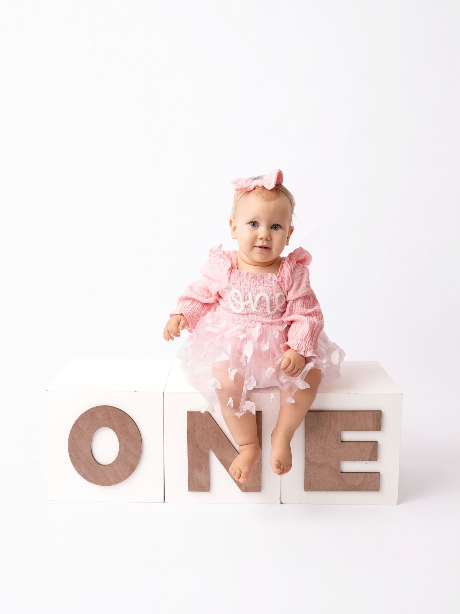 Baby girl in pink tutu dress sits on ONE letter blocks for her first birthday photo session.