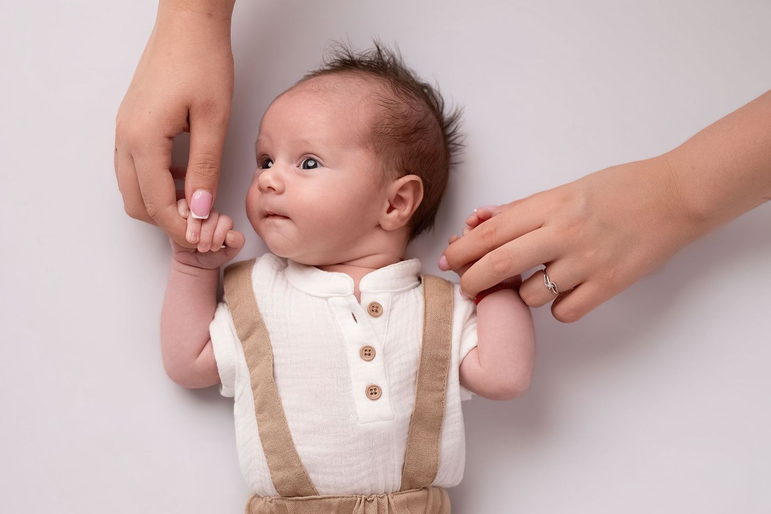 Newborn baby in suspenders held by mother's hands on white background.
