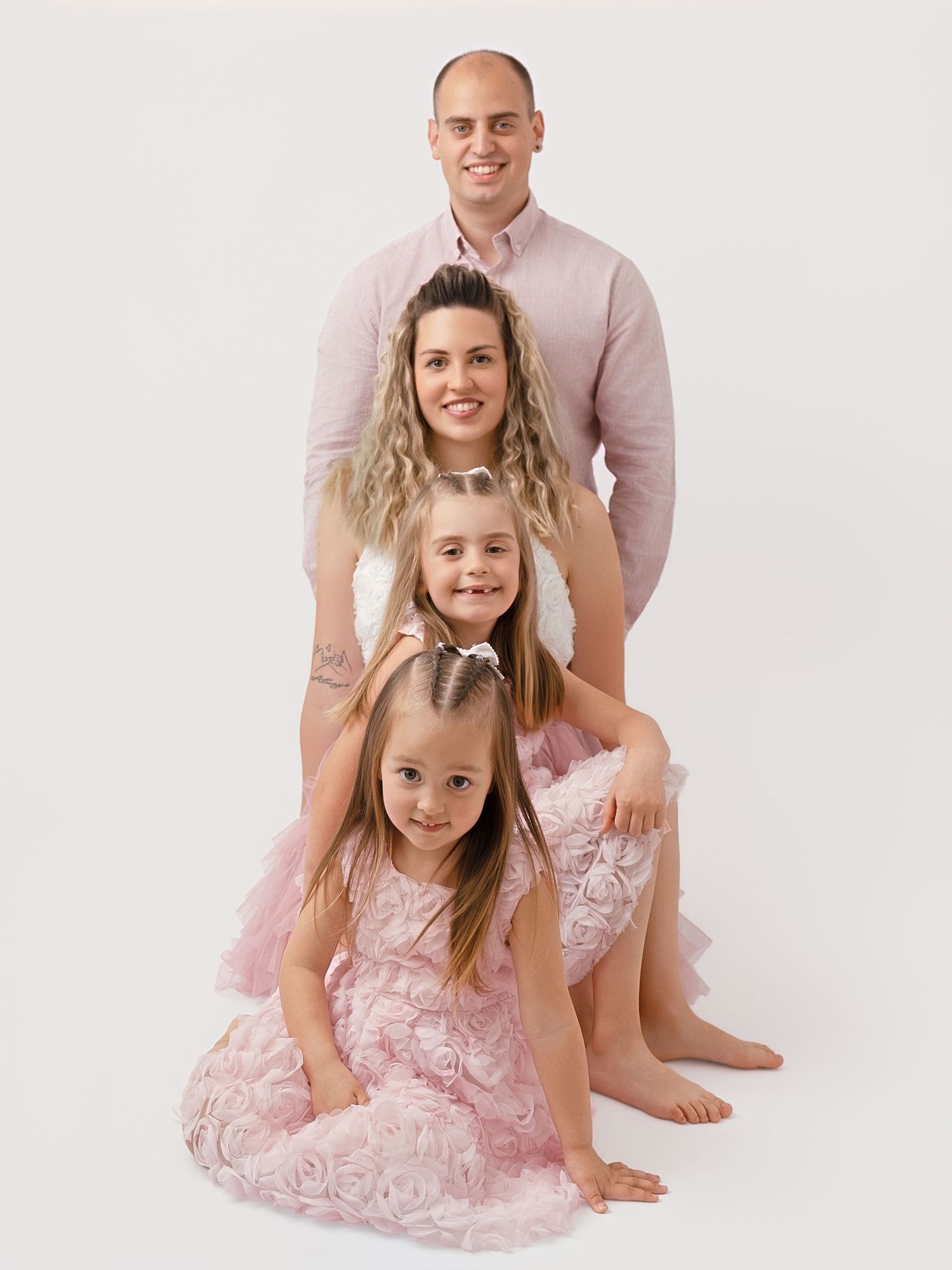 Family of four in matching pink outfits posing together in a bright studio portrait session.