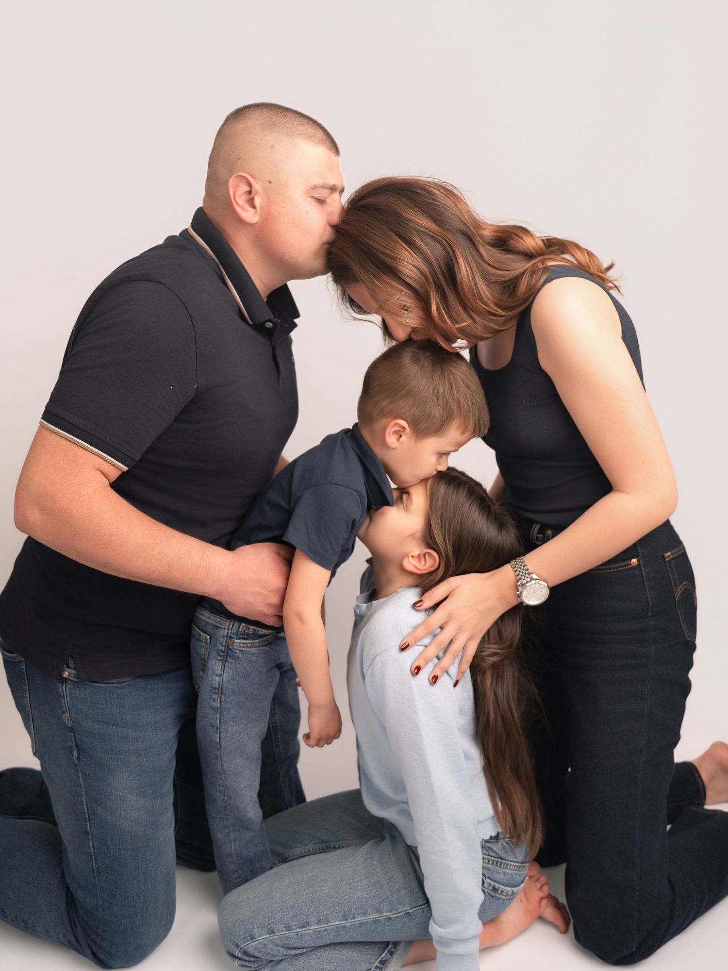 Family portrait of parents kissing while two children huddle together in a warm studio photo session.
