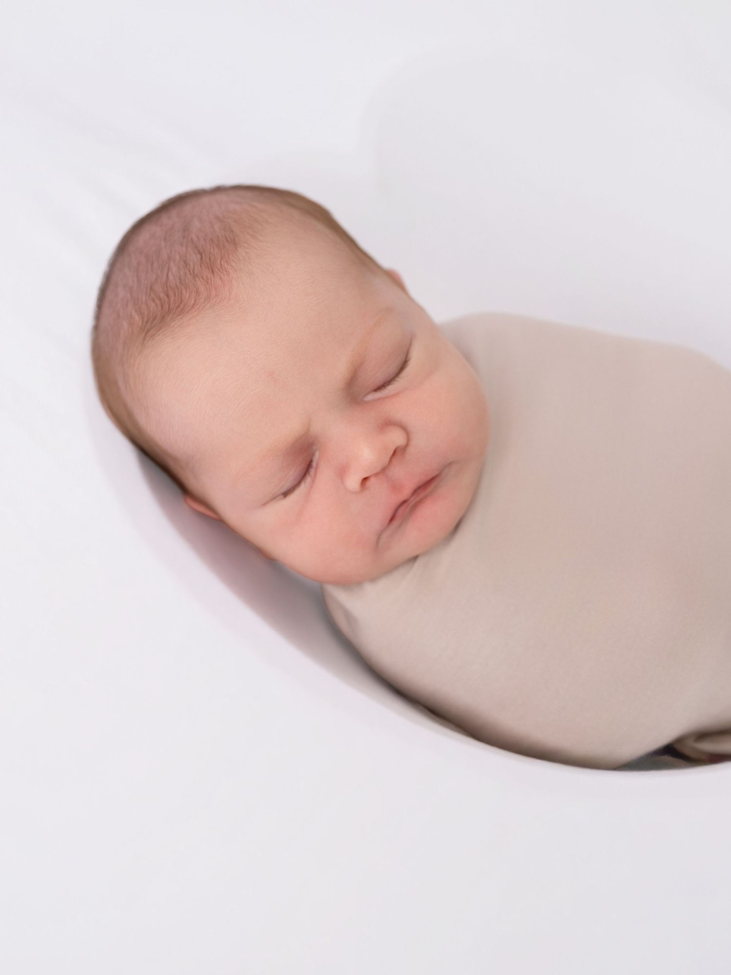 Peacefully sleeping newborn baby swaddled in a soft beige wrap on a white background.