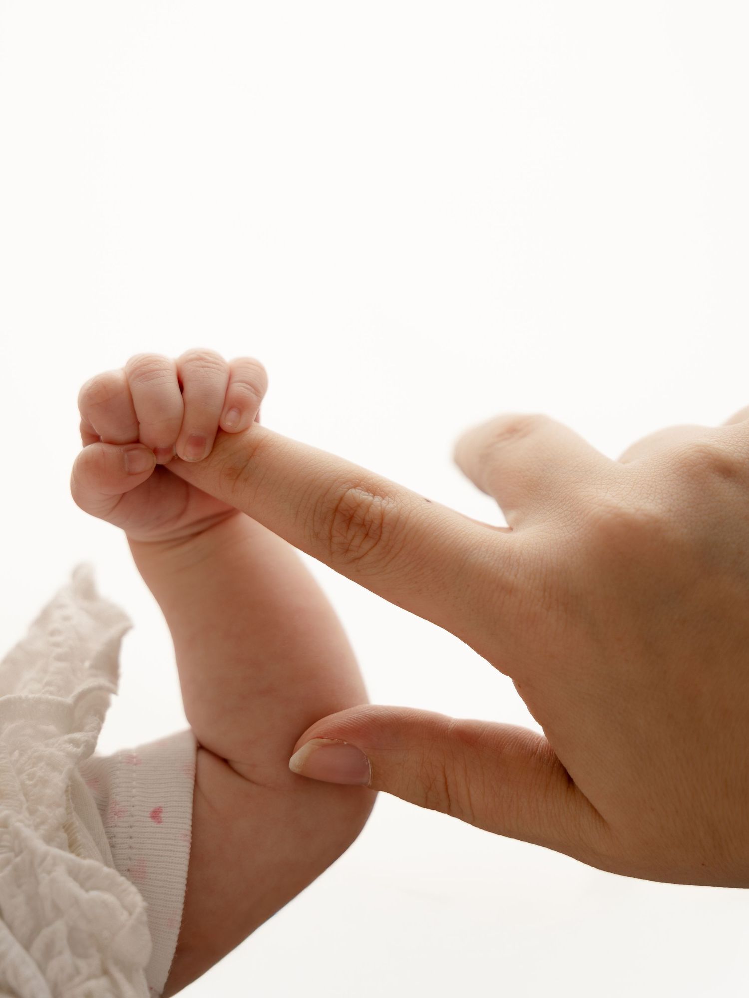 Newborn baby fist gripping adult finger tightly.
