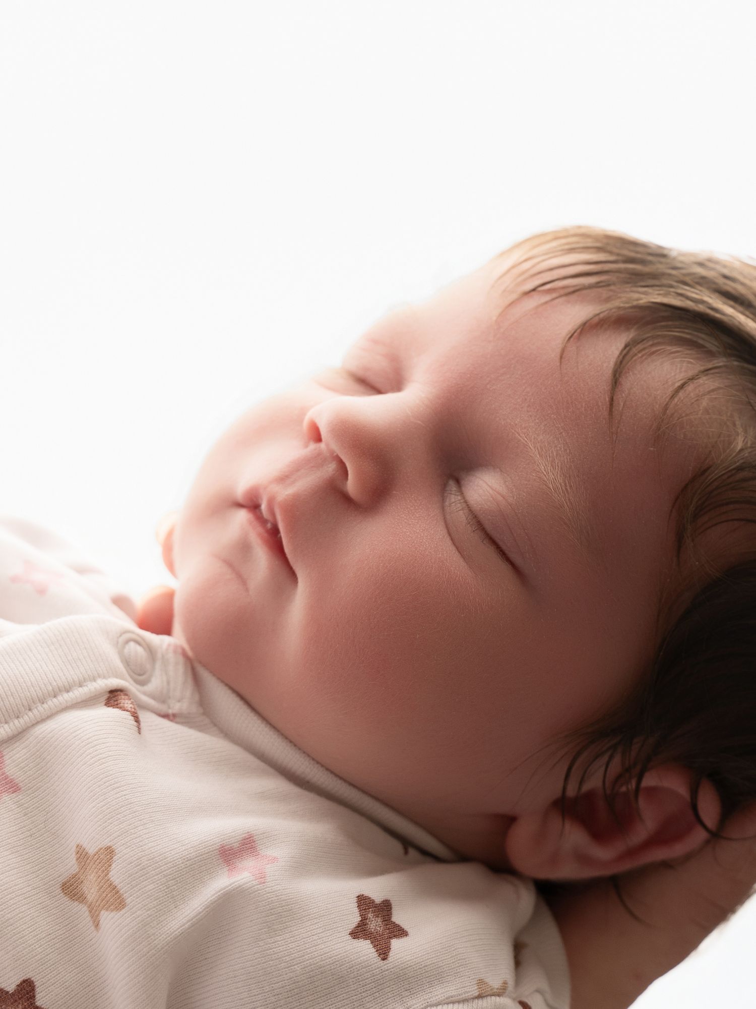 Peaceful sleeping newborn baby in star-print onesie with soft light illuminating delicate features.