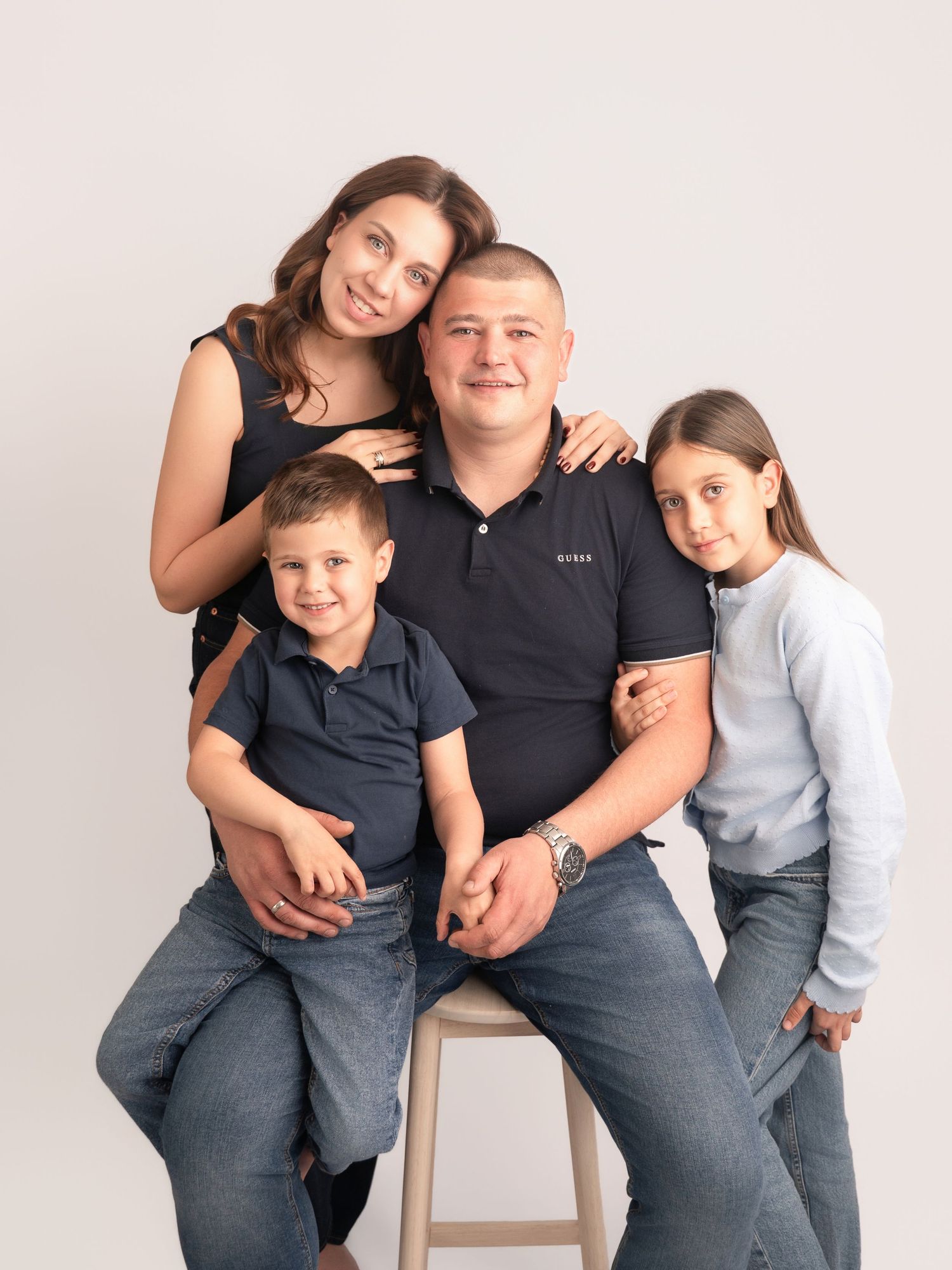 Happy family of four posing together in a studio, parents with two children smiling warmly against a light background.