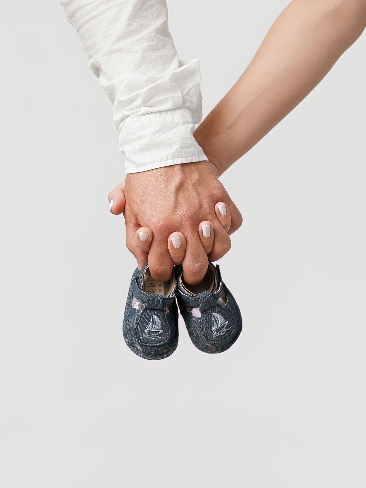 Two hands holding tiny baby shoes together, symbolizing pregnancy and parenthood anticipation.