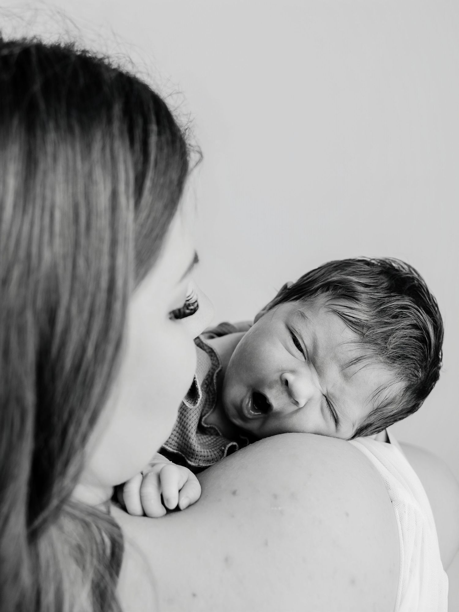 Black and white close-up of mother holding crying newborn baby on her shoulder lovingly.