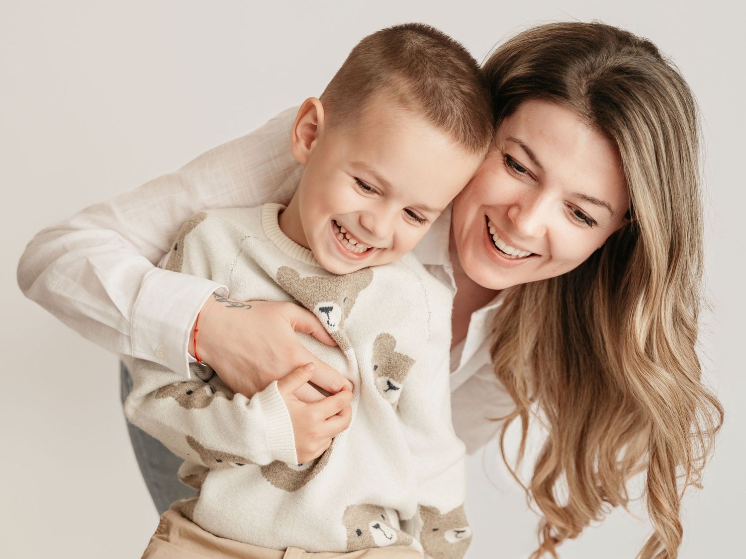Joyful mother and young son laughing together in casual matching outfits during studio portrait.