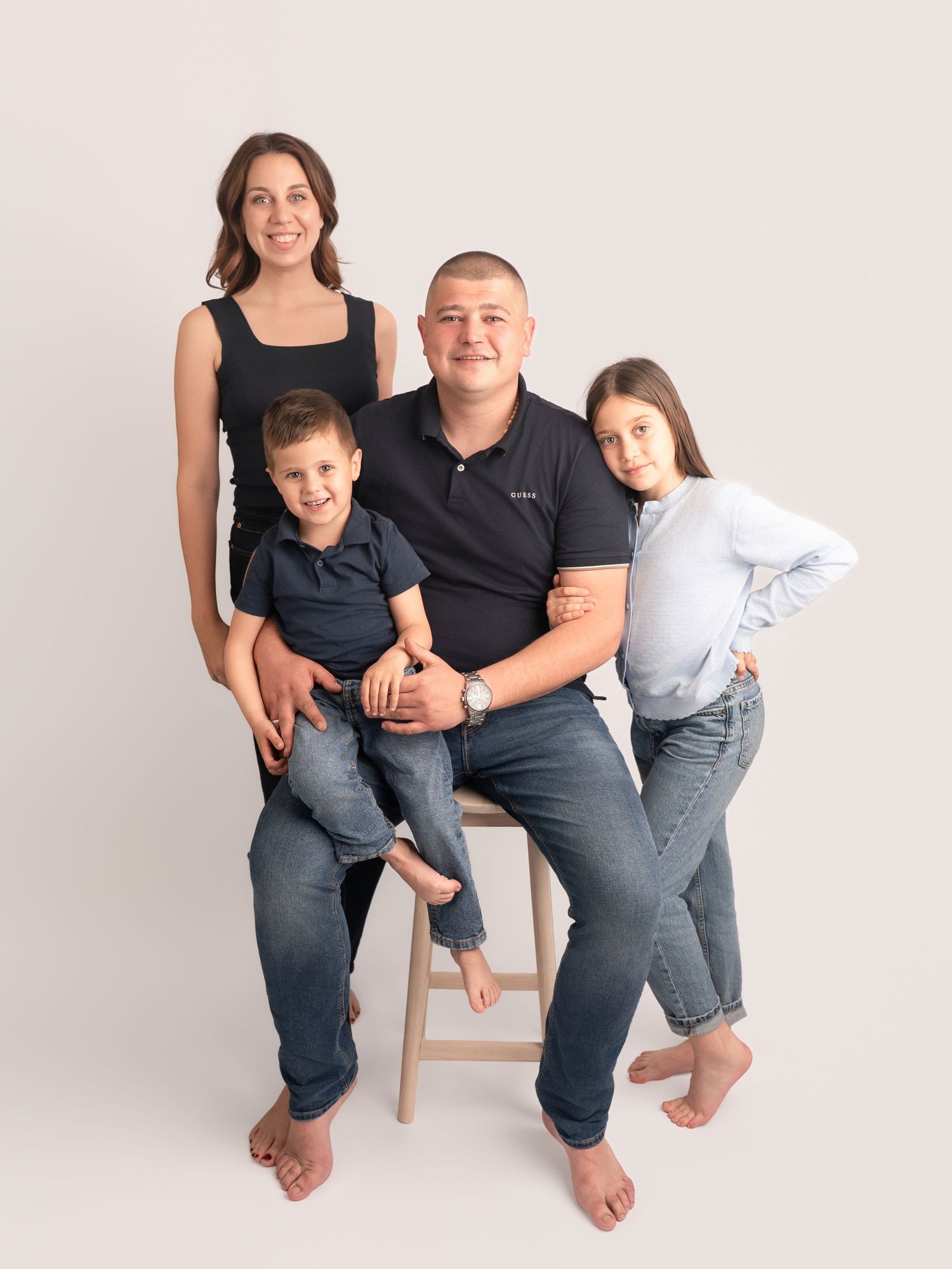 Family of four posing for a studio portrait, parents with two children smiling against a white background.