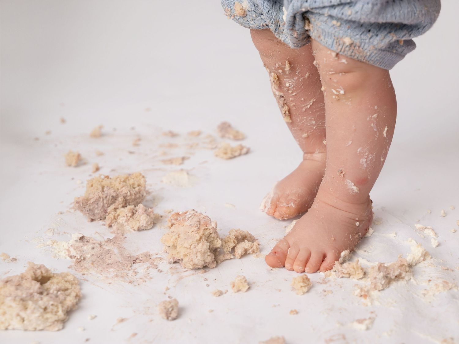 Baby feet covered in smash cake crumbs on white floor after first birthday.