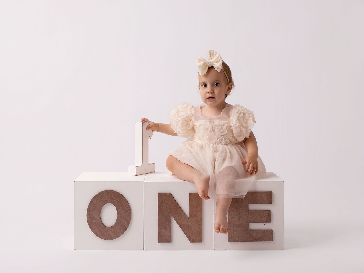 Baby girl in cream dress sits on white ONE blocks for her first birthday photo session.