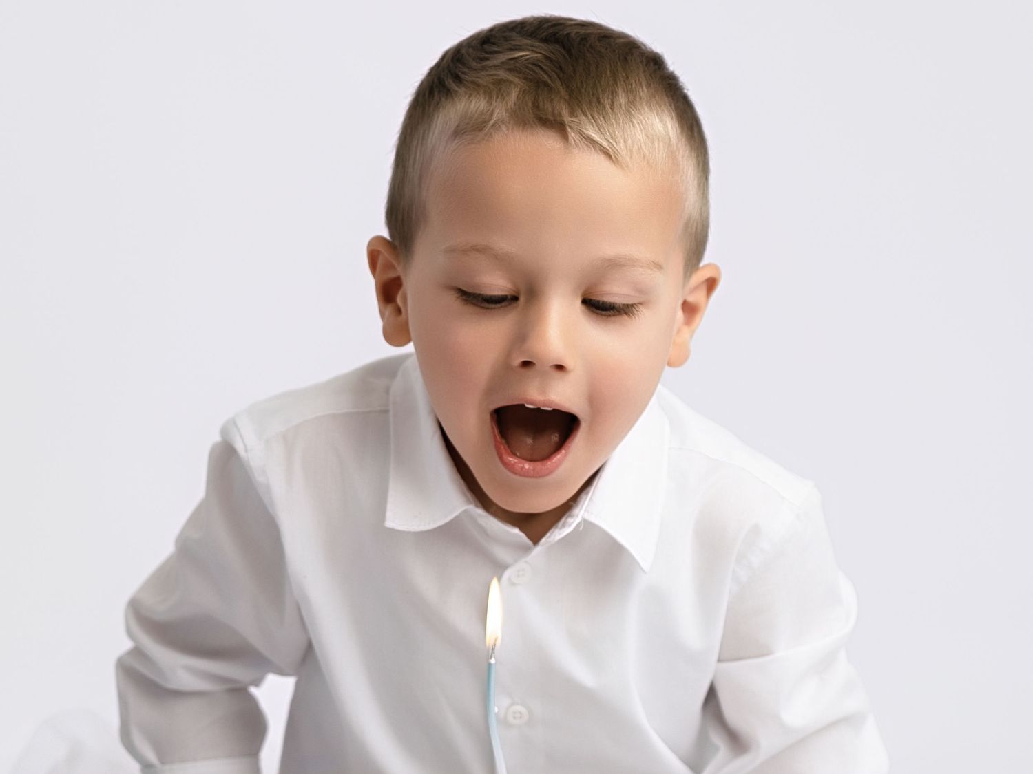 Excited young boy in white shirt with mouth open in surprise against light gray background.