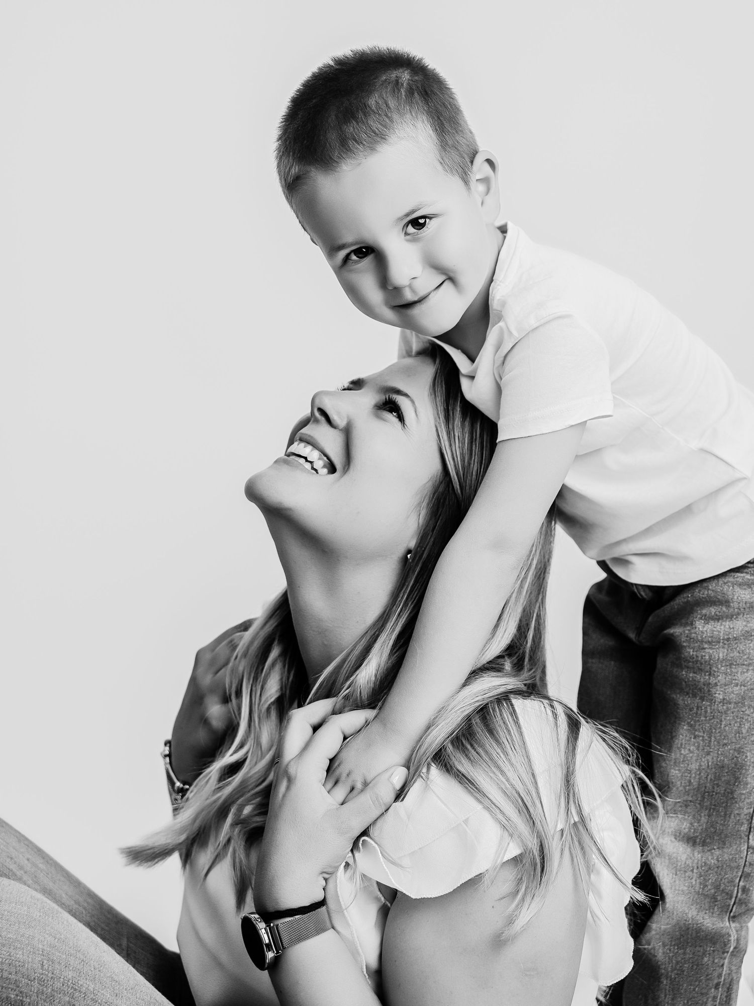 Black and white portrait of a smiling mother looking up at her young son who rests on her shoulders.
