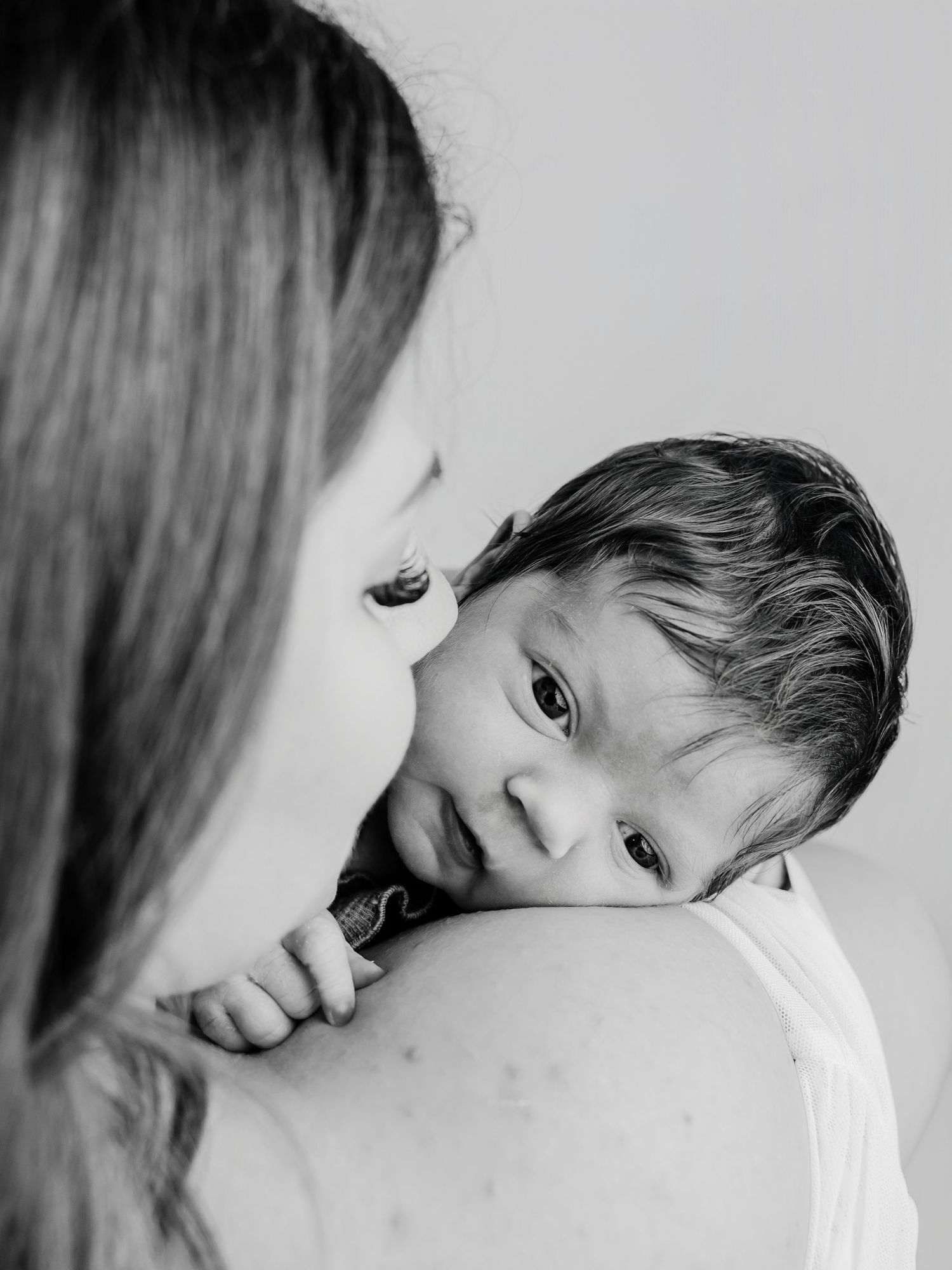 Black and white photo of mother holding alert newborn baby over her shoulder tenderly.