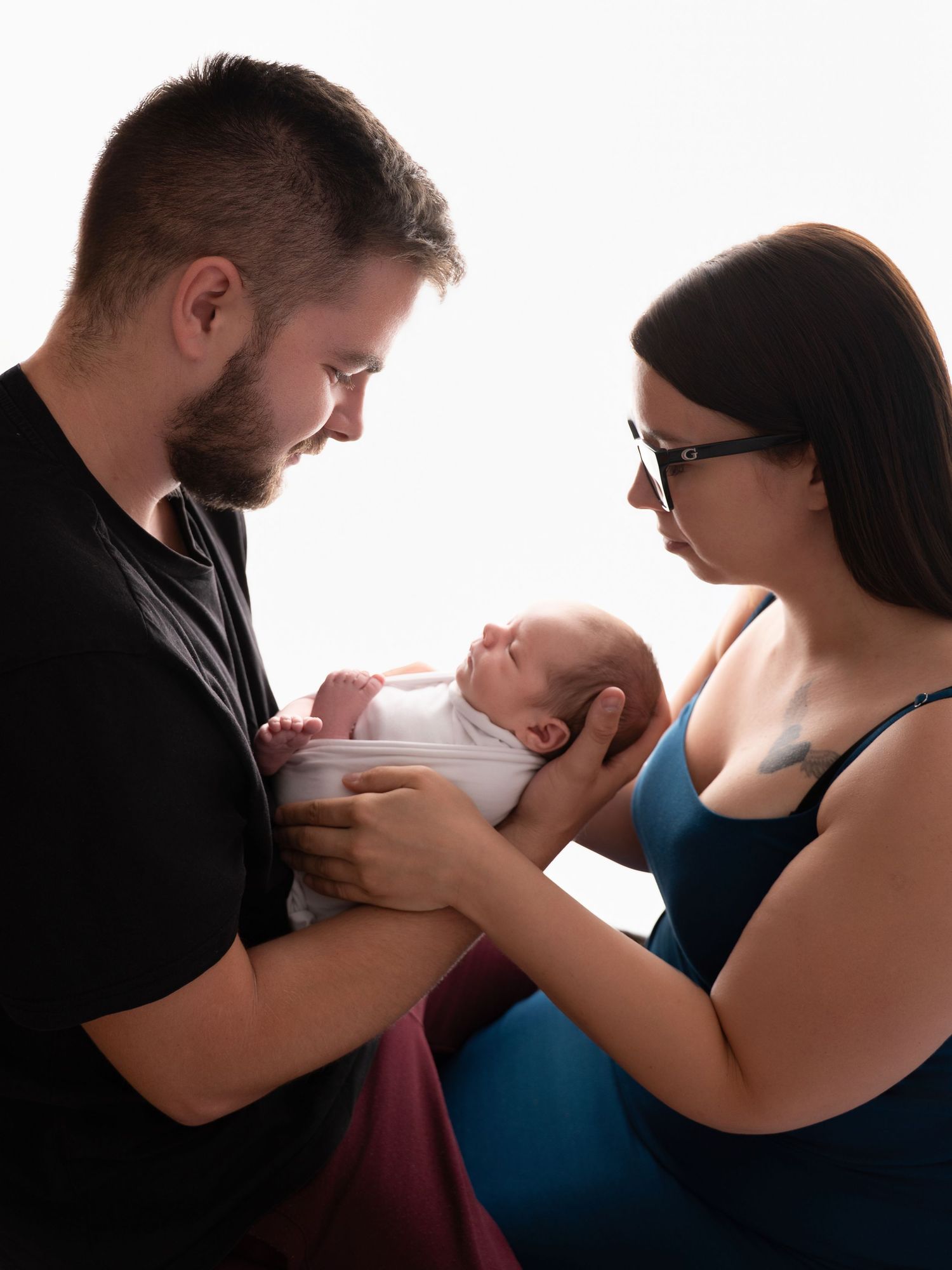 New parents lovingly gaze at their newborn baby in a bright studio portrait session.