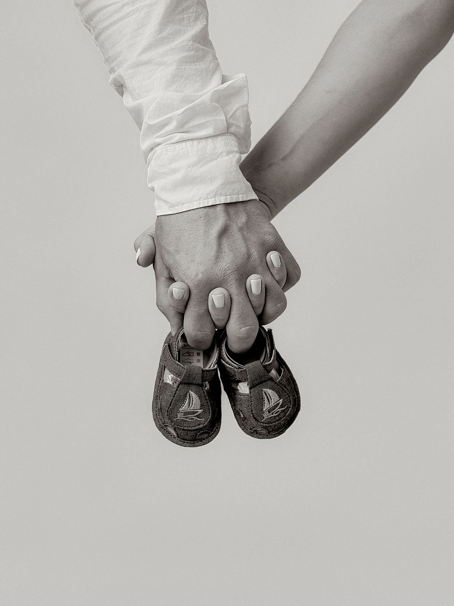 Two hands holding tiny baby shoes together in a black and white pregnancy announcement photo.