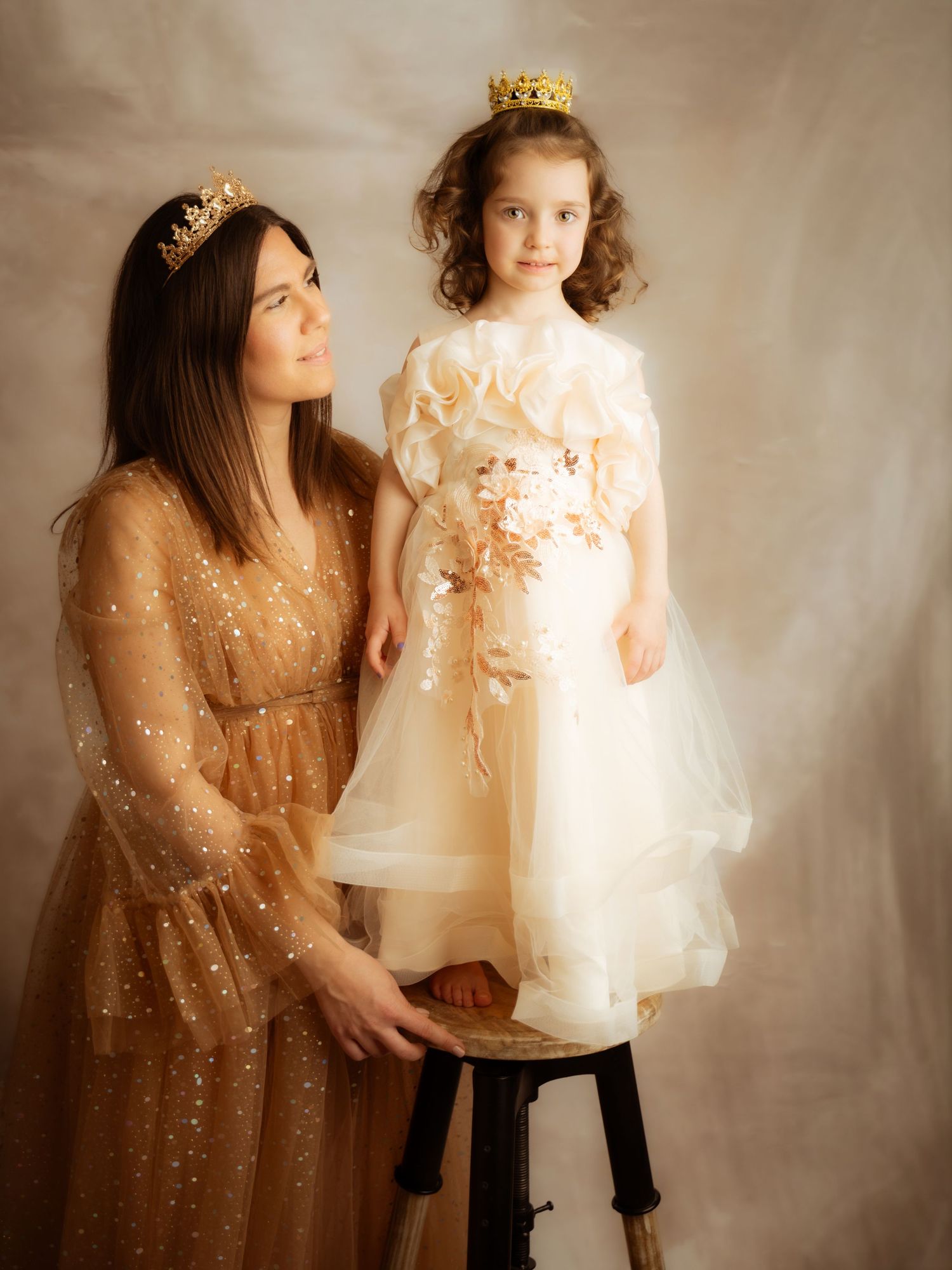 Woman and young girl both wearing gold crowns posing together in elegant tulle dresses.